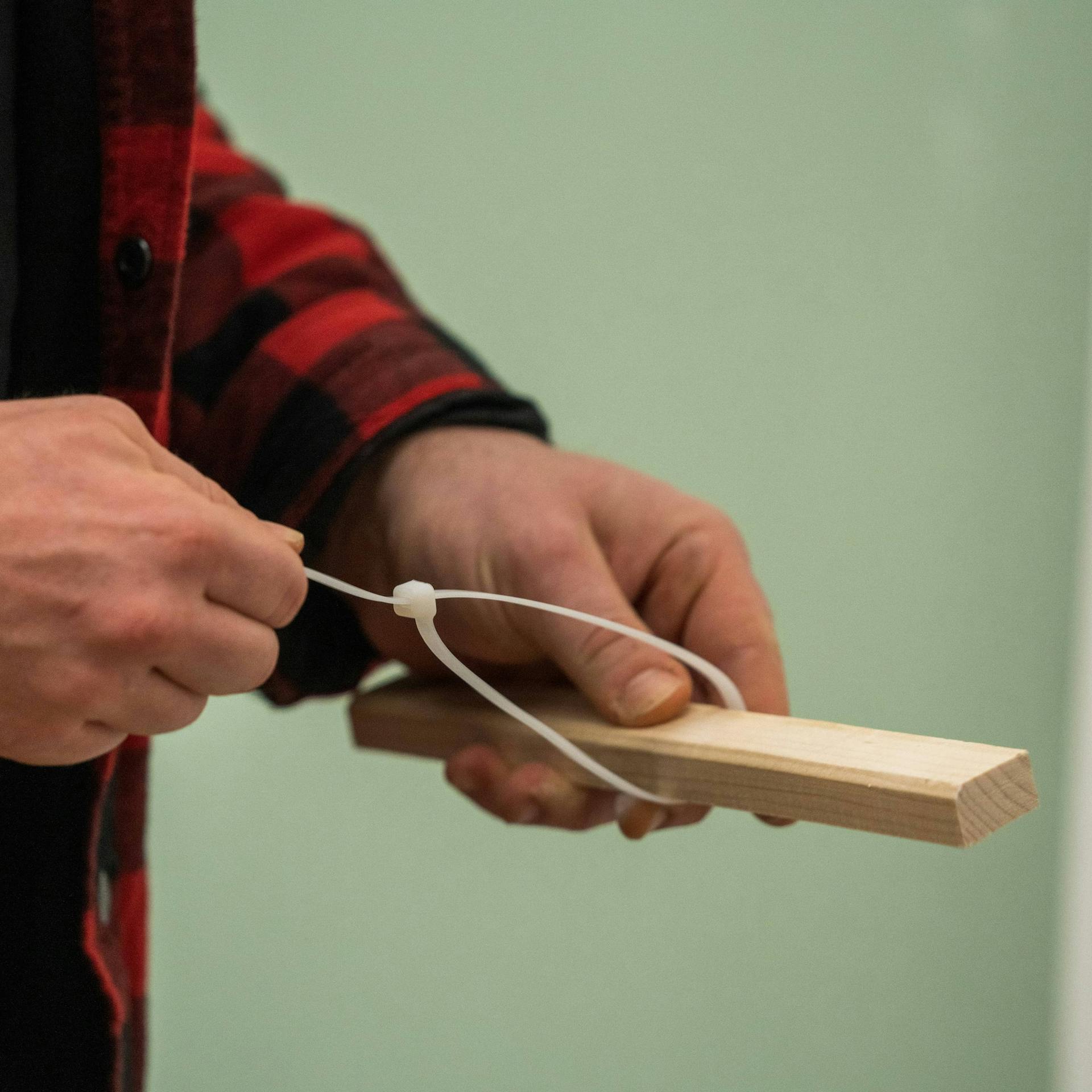 Jemand befestigt einen Kabelbinder an einer Holzlatte.