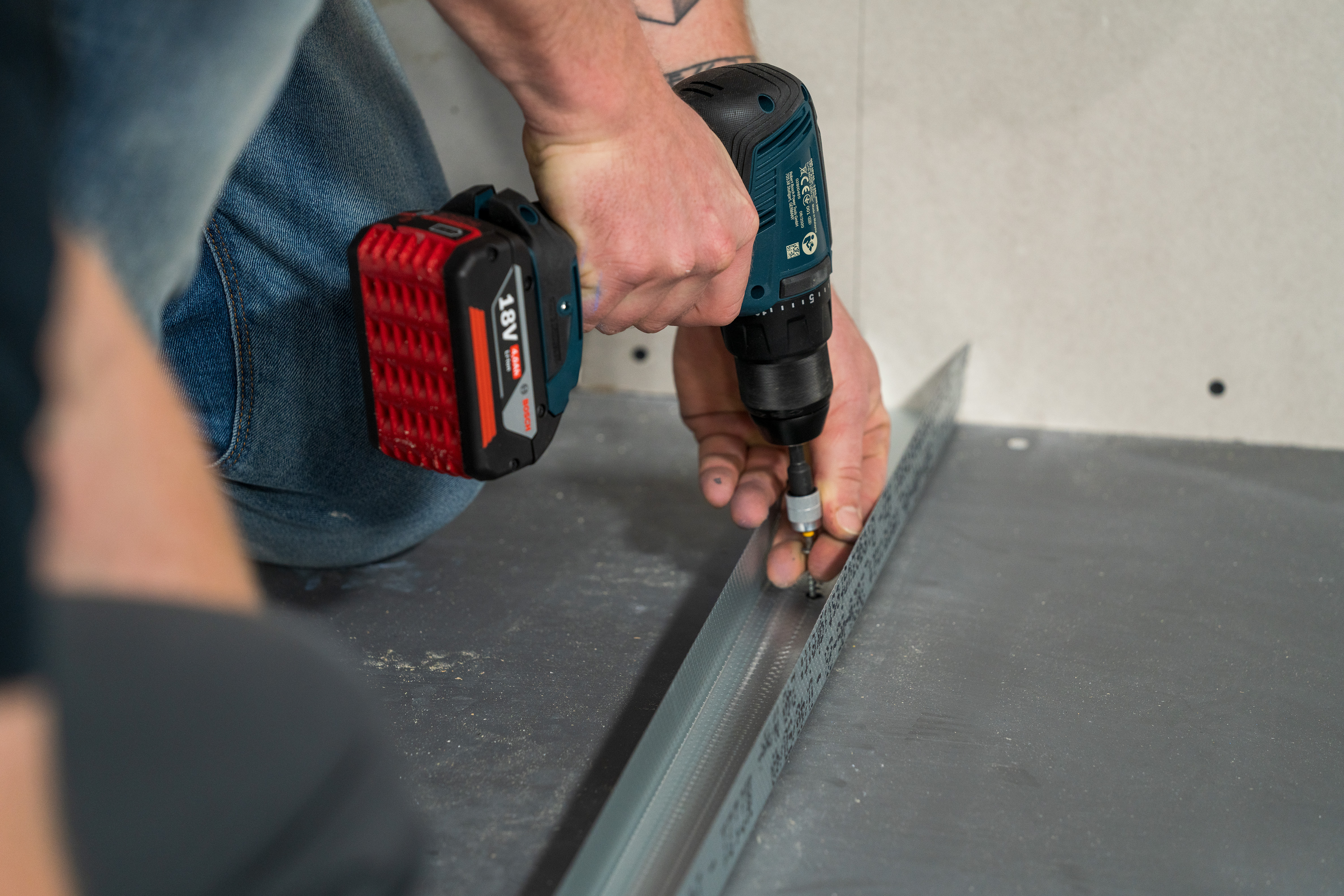 Domáci kutili napolohujú a priskrutkujú vyrezaný UW profil na dláždenú podlahu.