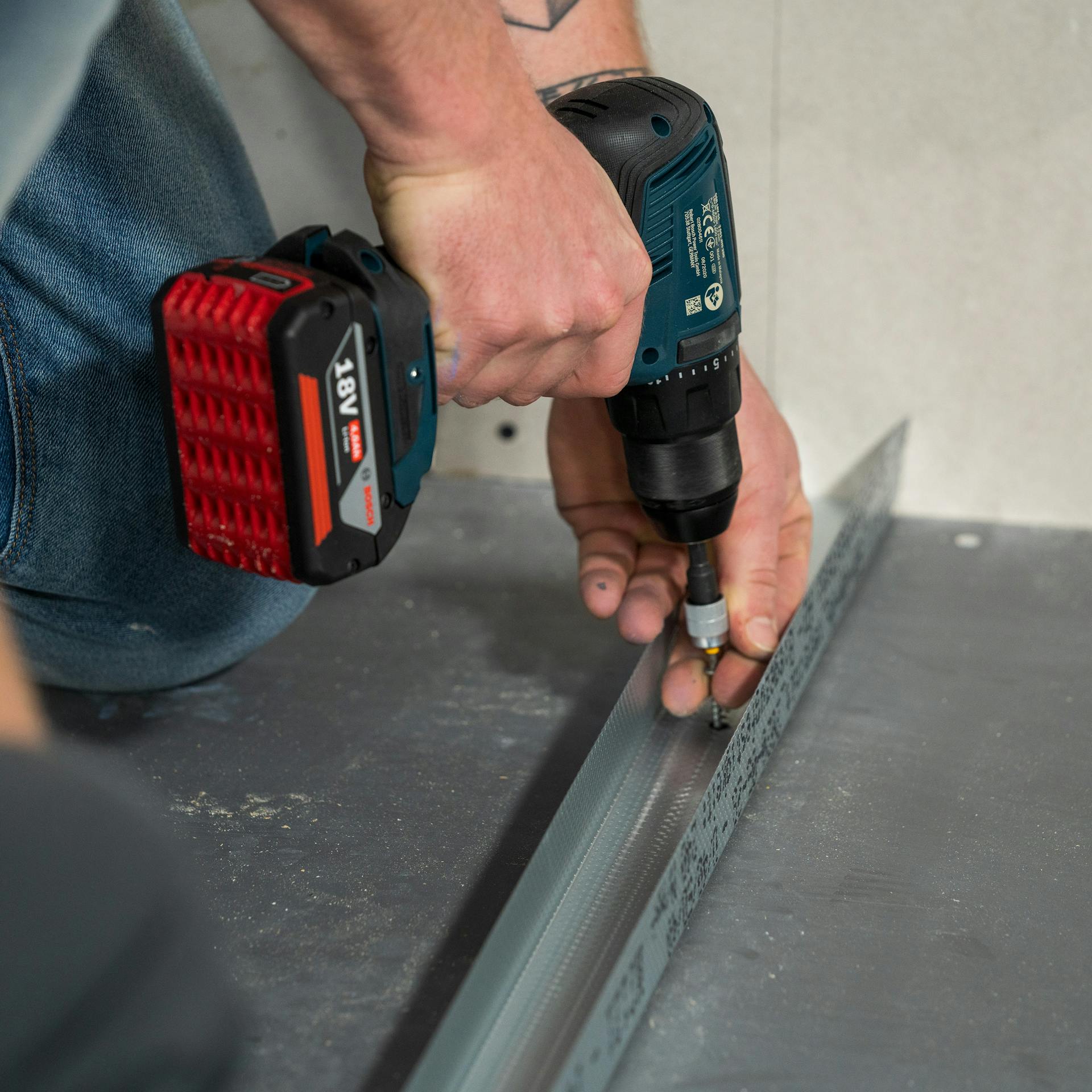 Heimwerker positioniert und verschraubt das zugeschnittene UW-Profil auf dem Fliesenboden.