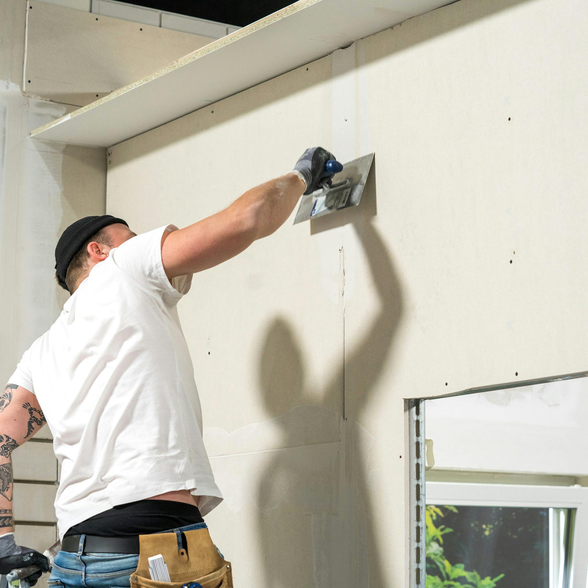 Remeselník tmel sadrokartón pomocou špachtle.