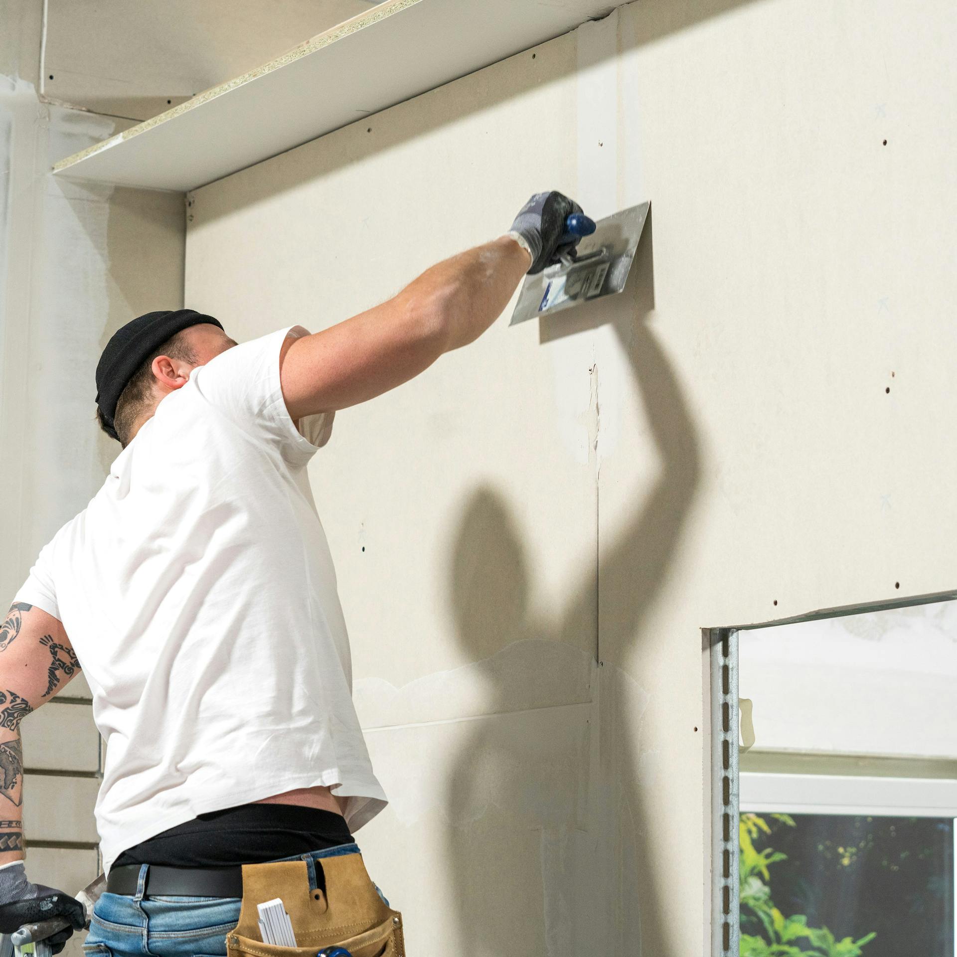 Un artigiano stucca la parete in cartongesso con una spatola.