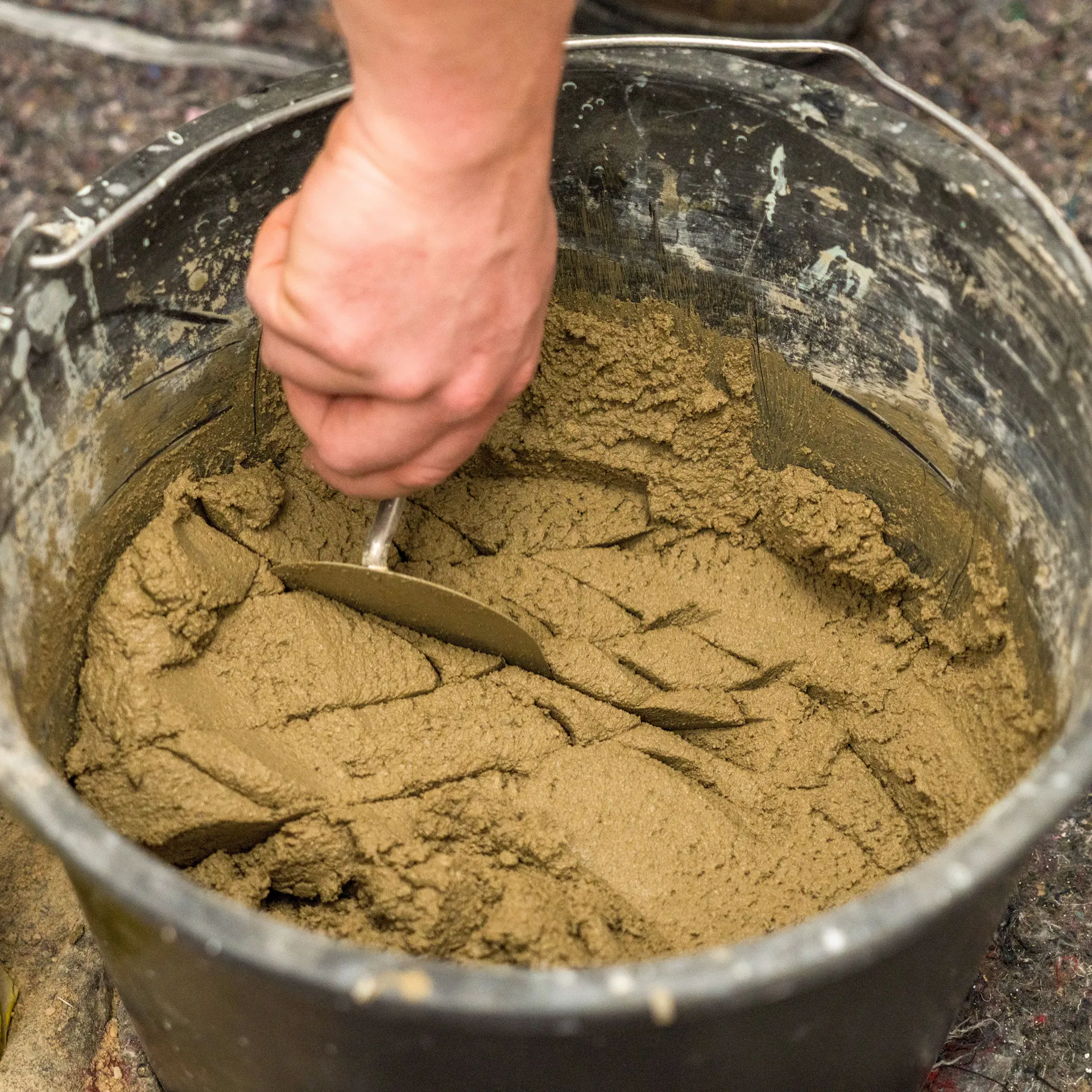 Handwerker nimmt Mörtel aus dem Eimer mit einer Kelle heraus.