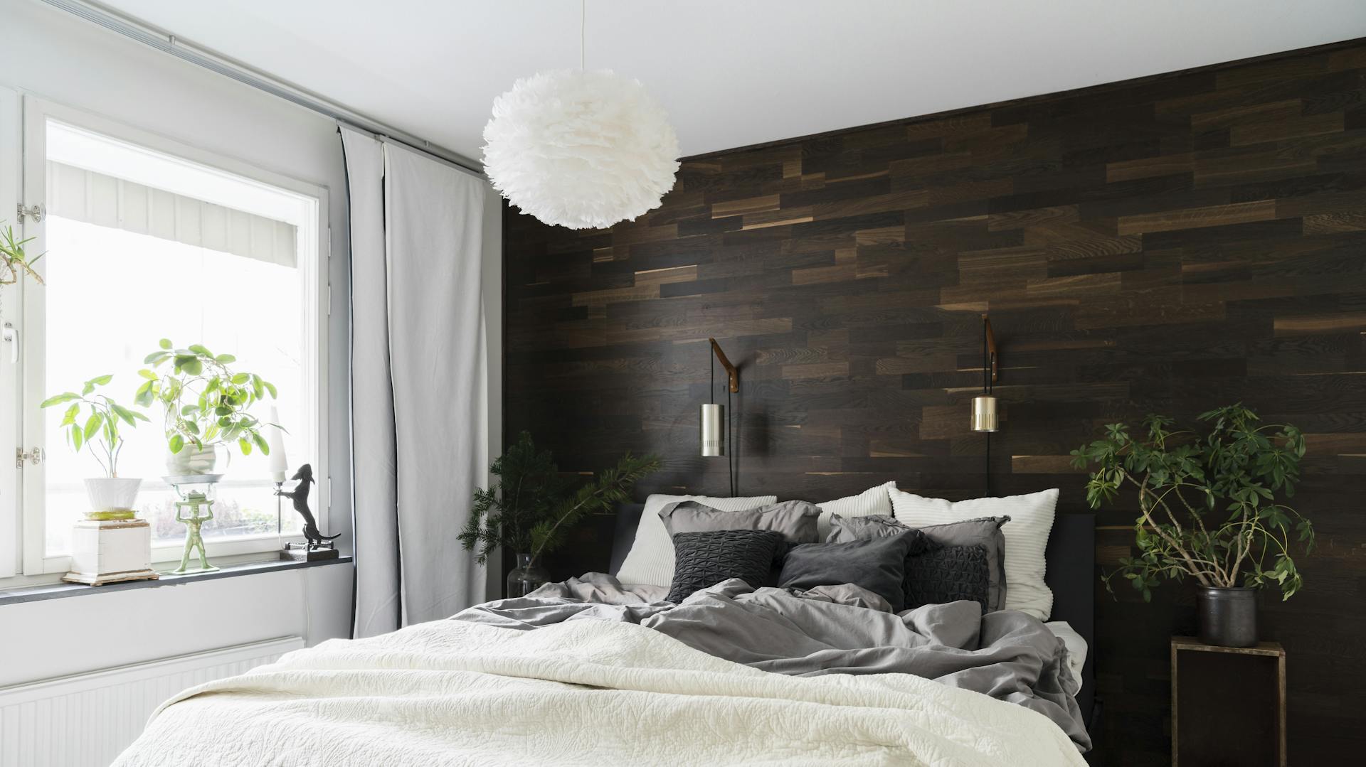 Schlafzimmer mit großem Bett und Beistelltisch vor einer dunklen Holzwand.