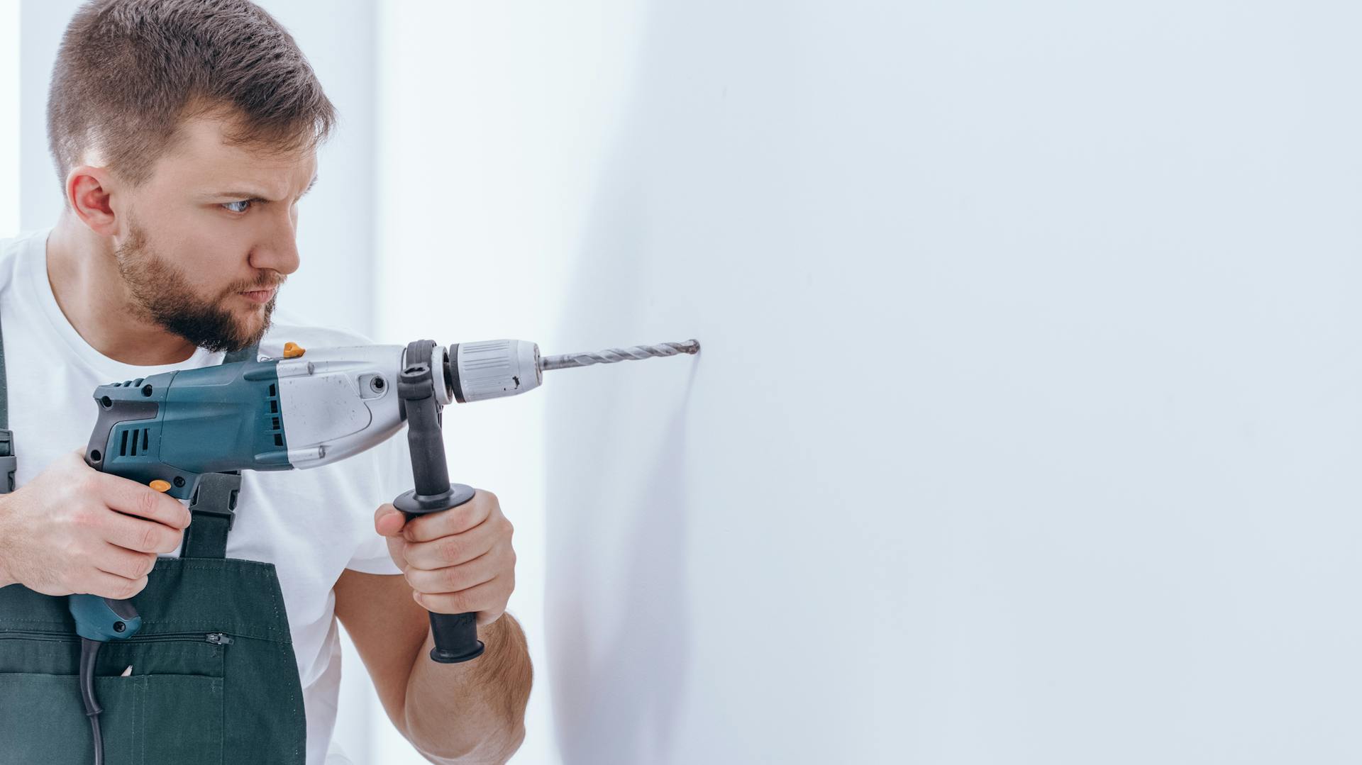 Mann entfernt Dübel mithilfe eines Bohrers aus der Wand