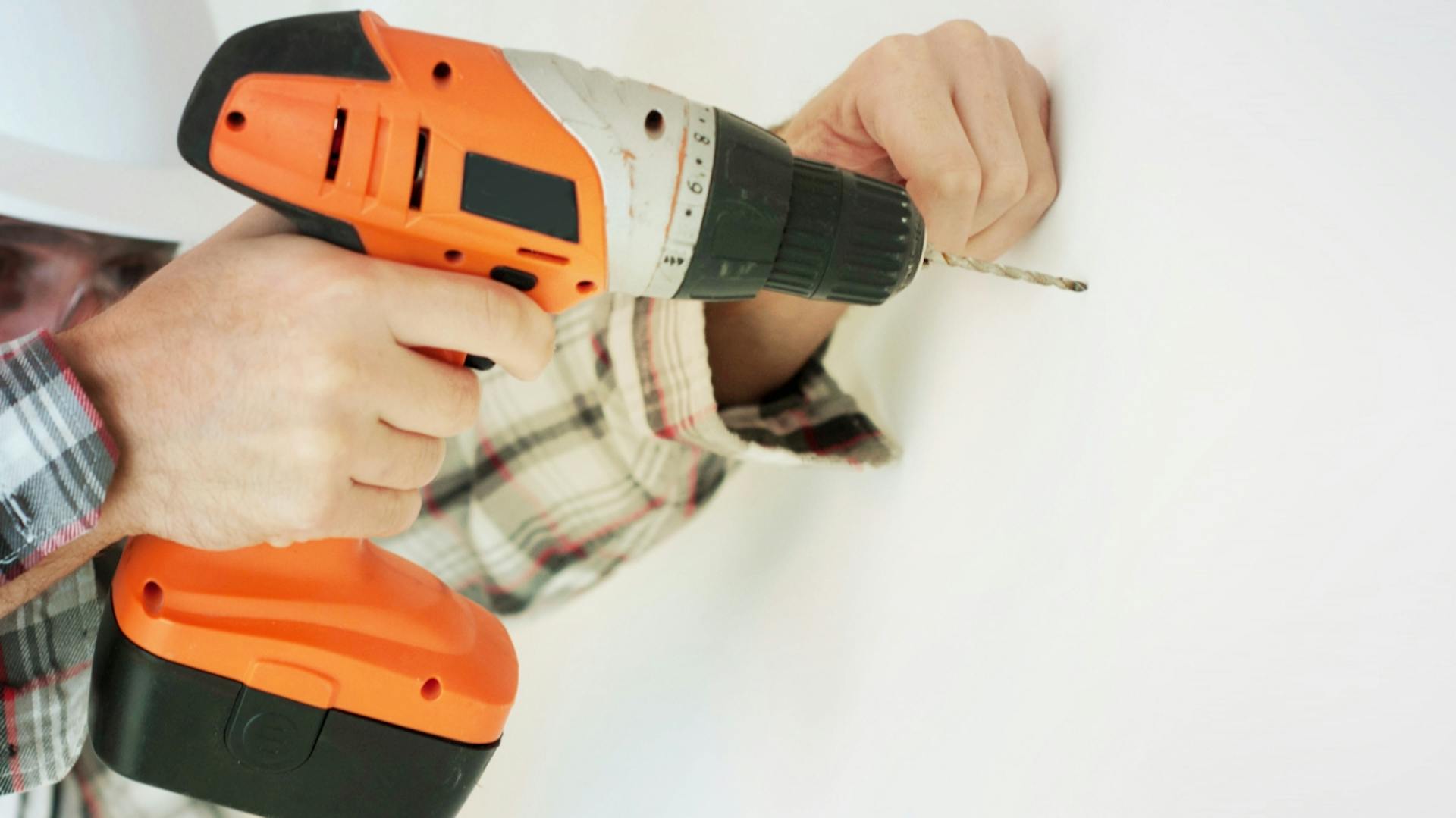 Muž prikladá oranžovú vŕtačku k stene