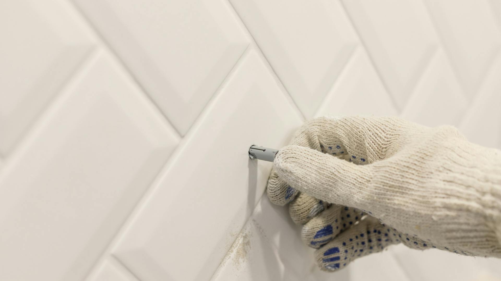 Jemand montiert einen Universaldübel in einer Wand mit Fliesenspiegel