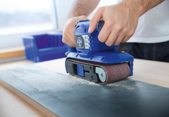 Egy ember egy kék csiszológéppel csiszol egy felületet.