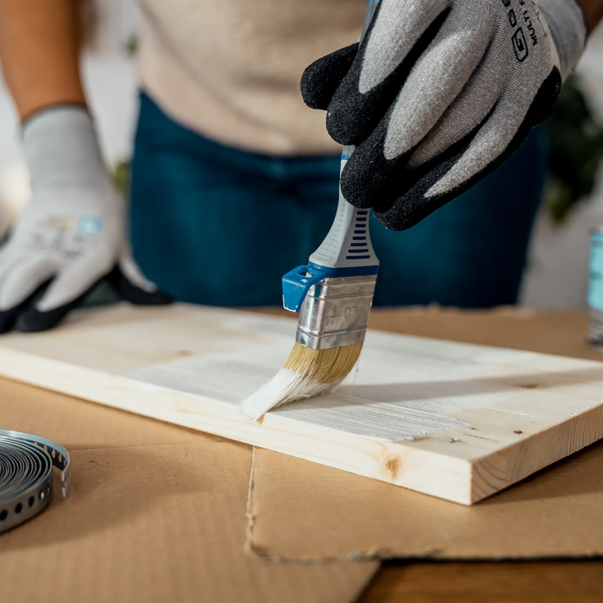 Con un pennello viene applicato uno strato sottile di vernice bianca sul legno naturale.