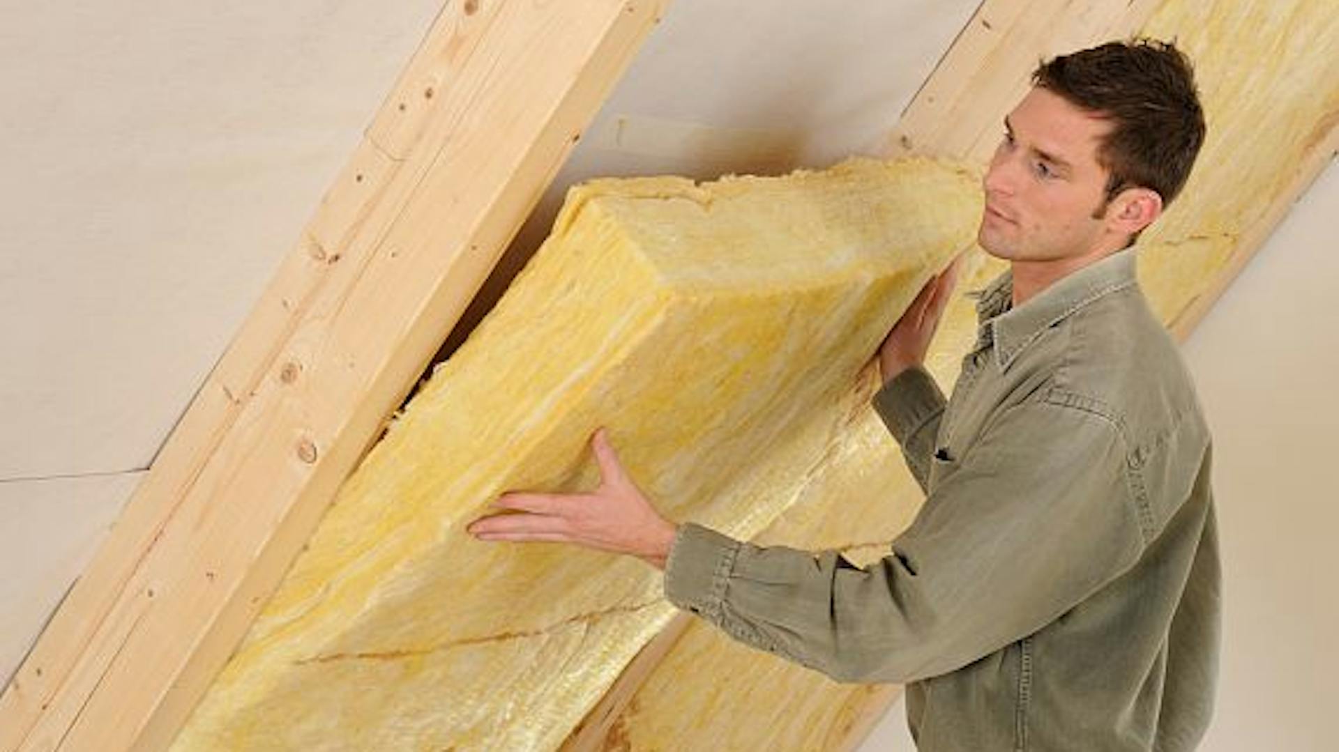 Az ezermester szigetelőanyagot tesz a gerendák közzé a ferde tetőre .