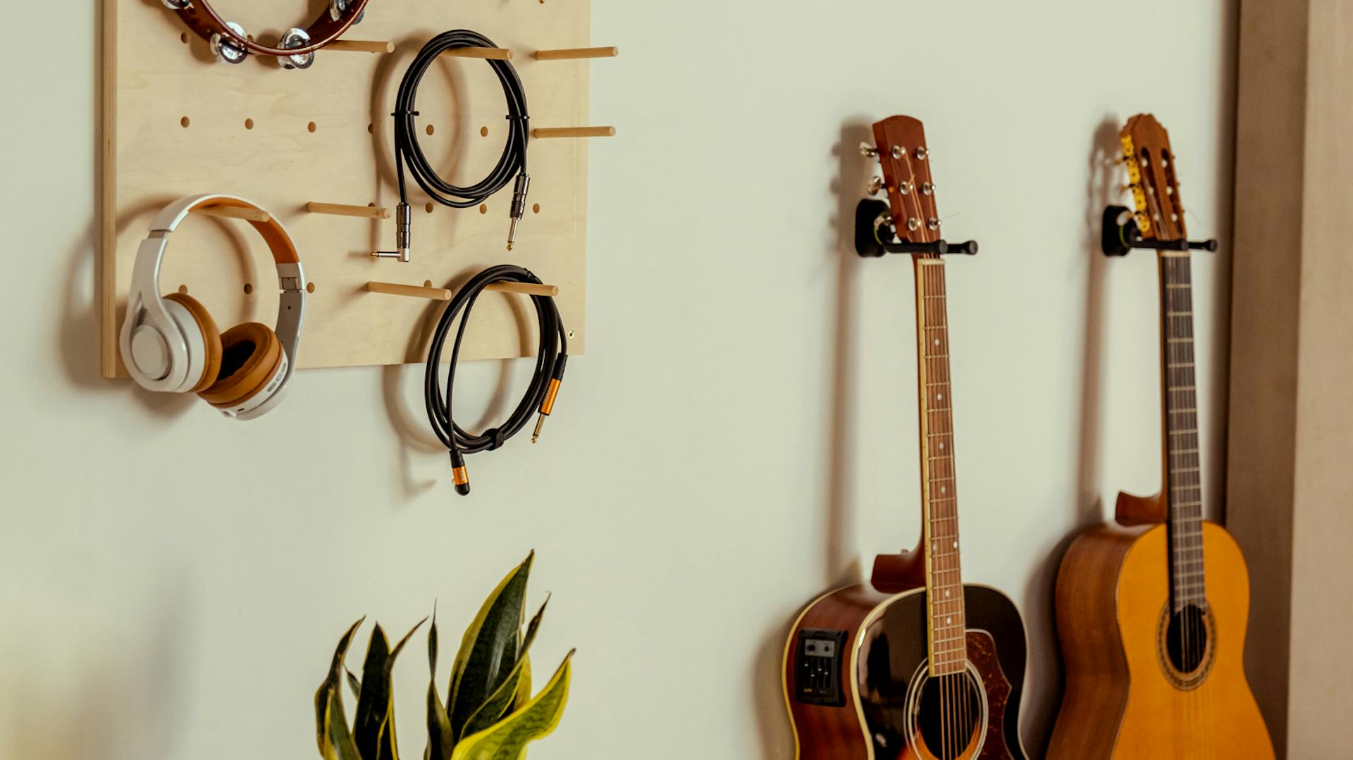 Kabel und Kophörer hängen an einem Pegboard, im Hintergrund hängen Gitarren.