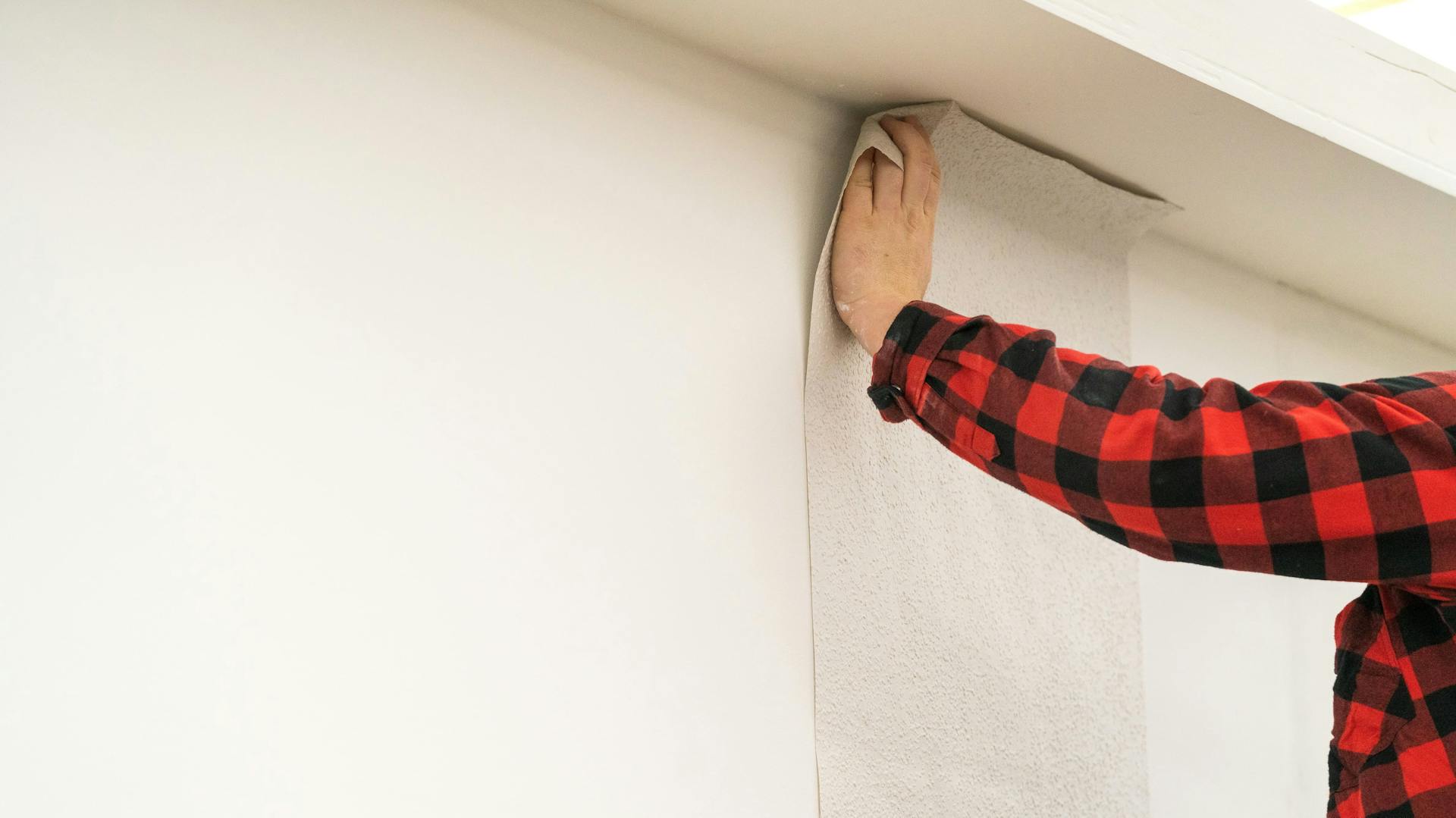 Person tapeziert Wand mit Raufaser.