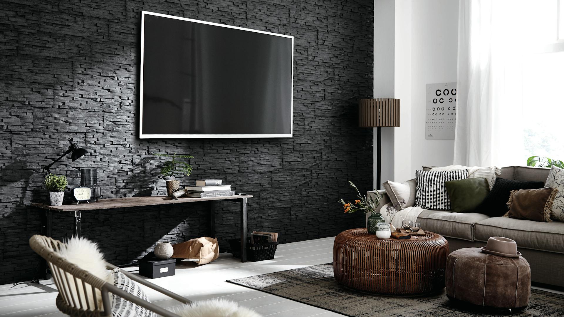 Ein modernes Wohnzimmer mit Steinwand in Anthrazit, Sofa, Sessel und Couchtischen.