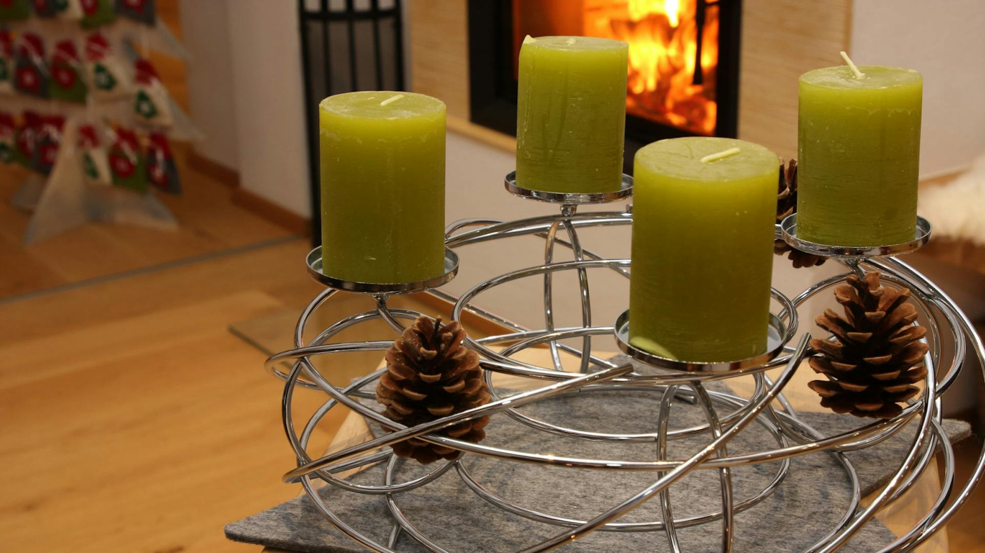 Corona dell’Avvento realizzata con aste di metallo, con candele verdi e coni d’abete in un salotto con caminetto sullo sfondo