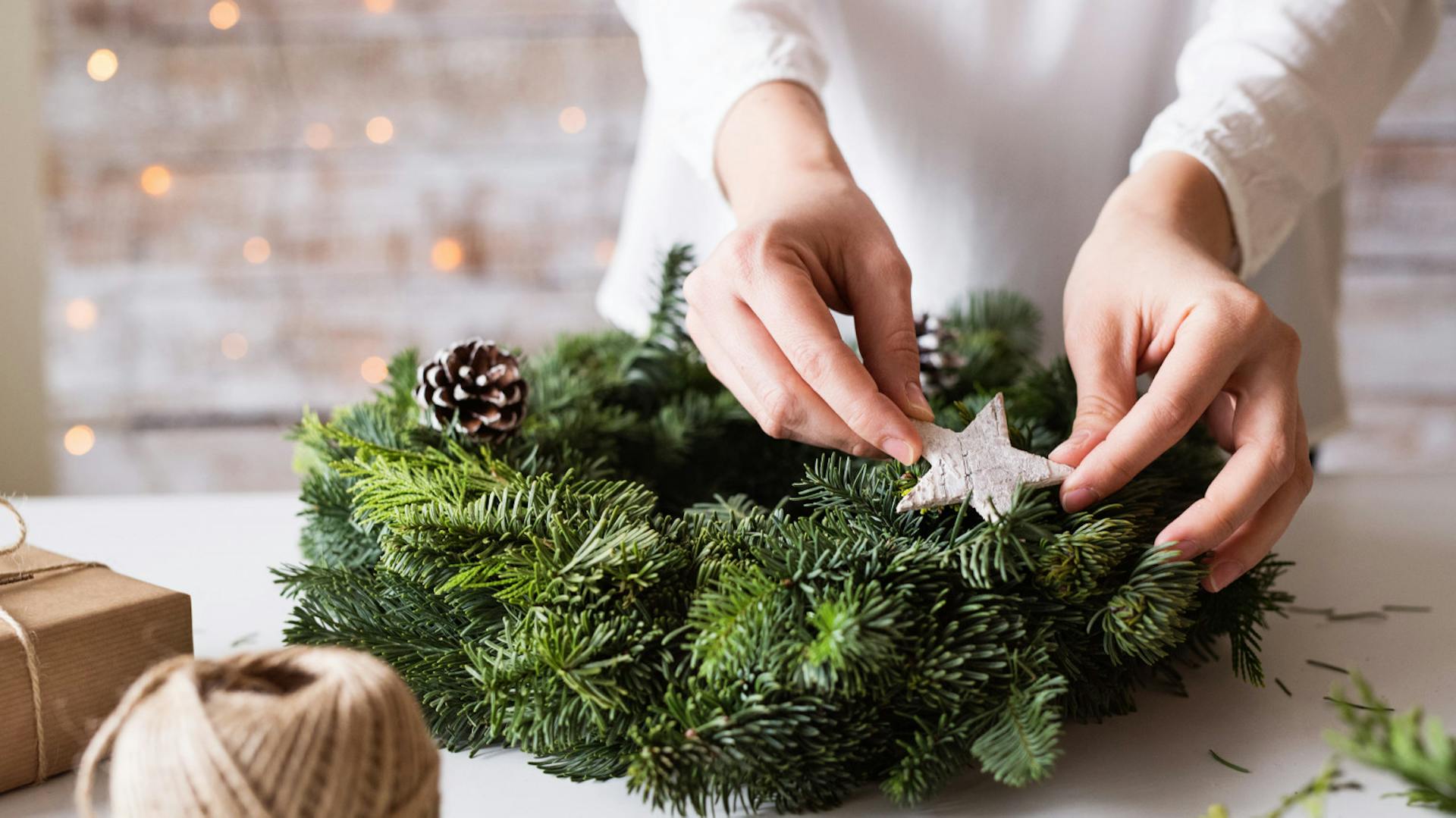 Donna mette stelle decorative argentate su corona dell’Avvento con ramoscelli d’abete verdi