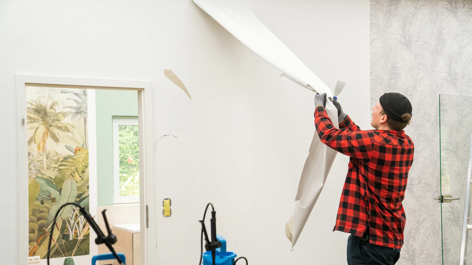 Heimwerker entfernt alte Tapete von Wand.