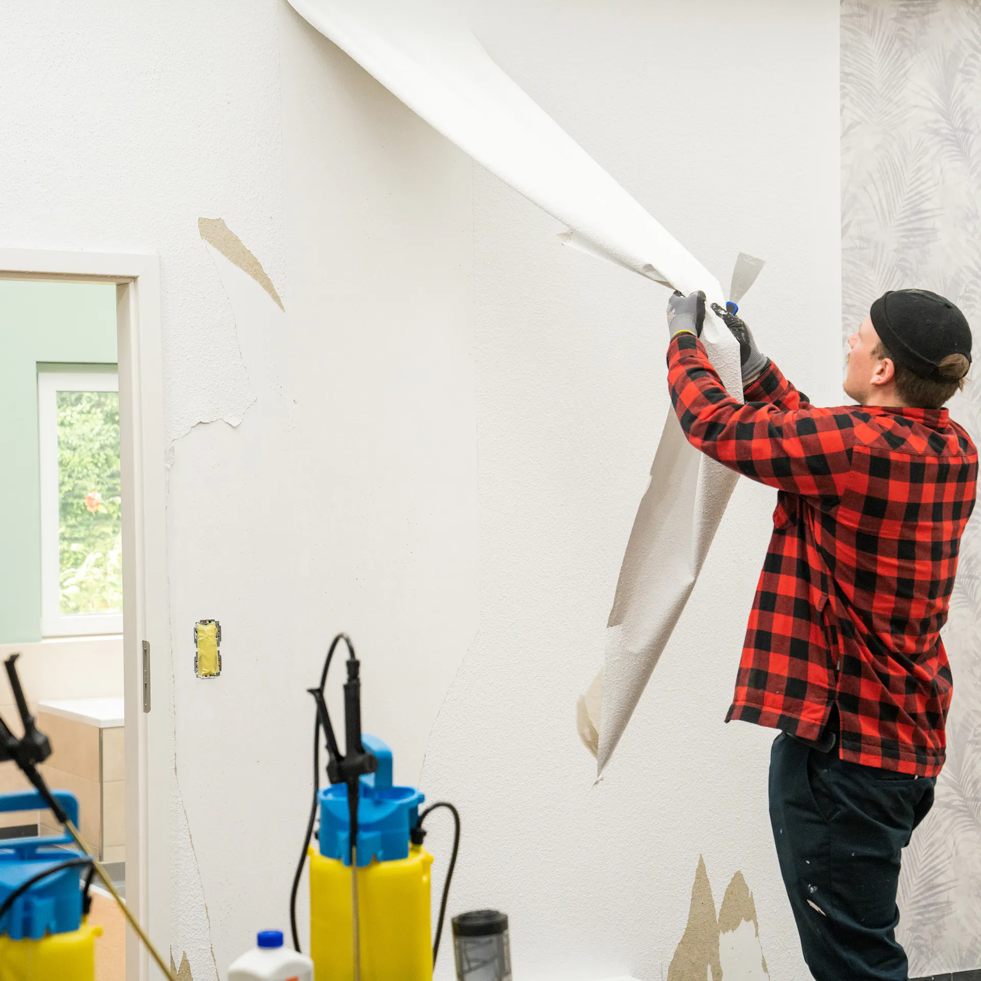 Mann entfernt Tapete von der Wand.