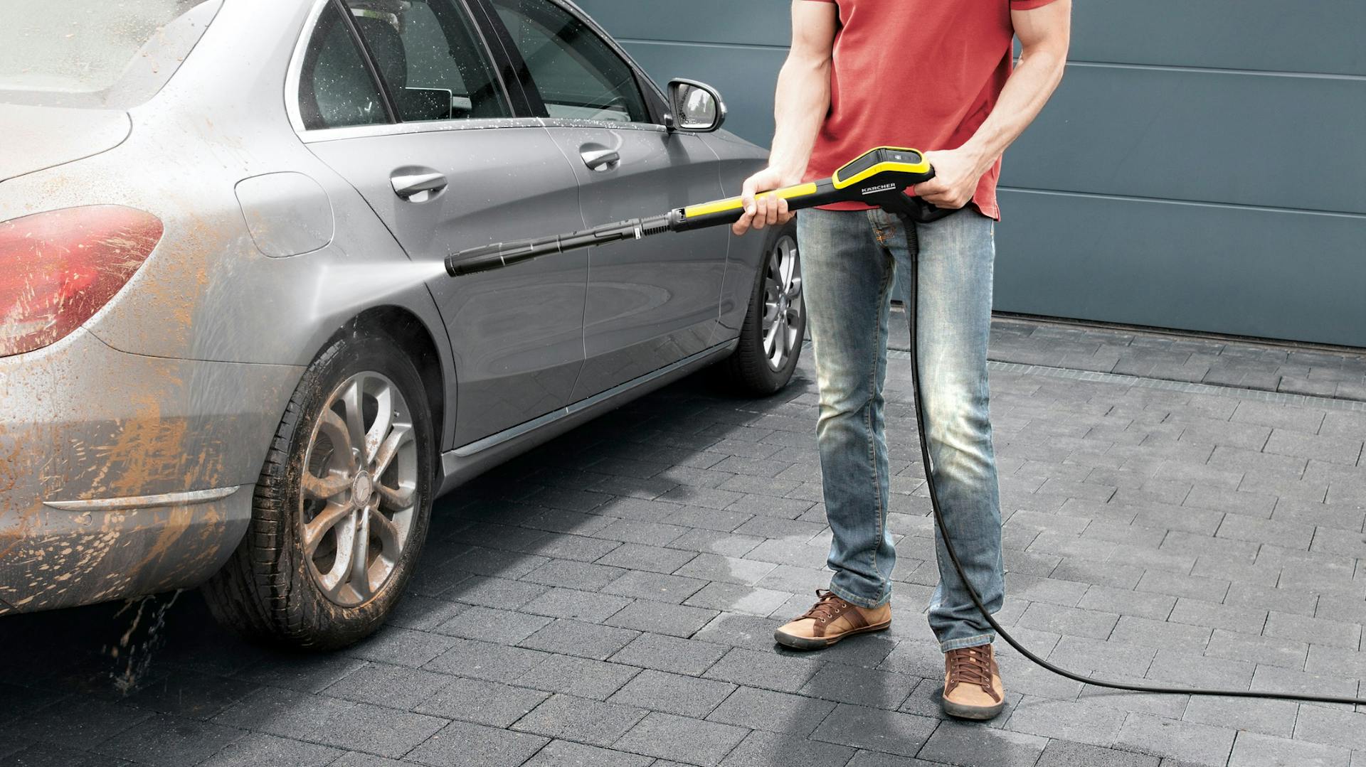 Mann löst groben Schmutz mit Hochdruckreiniger vom Auto.