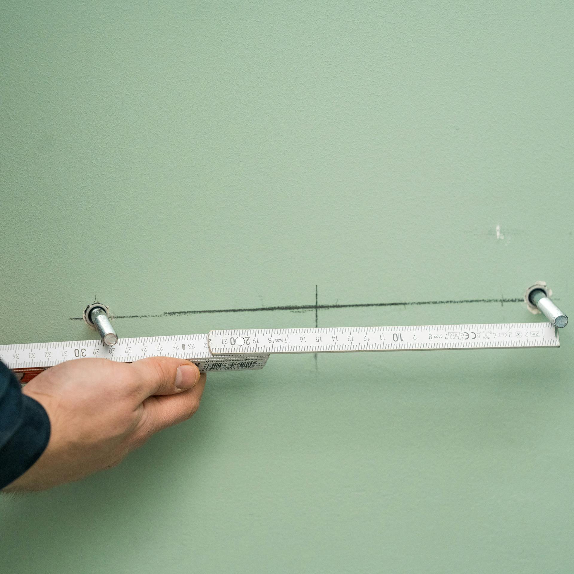 Heimwerker benutzt Wasserwaage, um später mit nebenliegendem Bohrer Löcher für Stockschrauben zu bohren