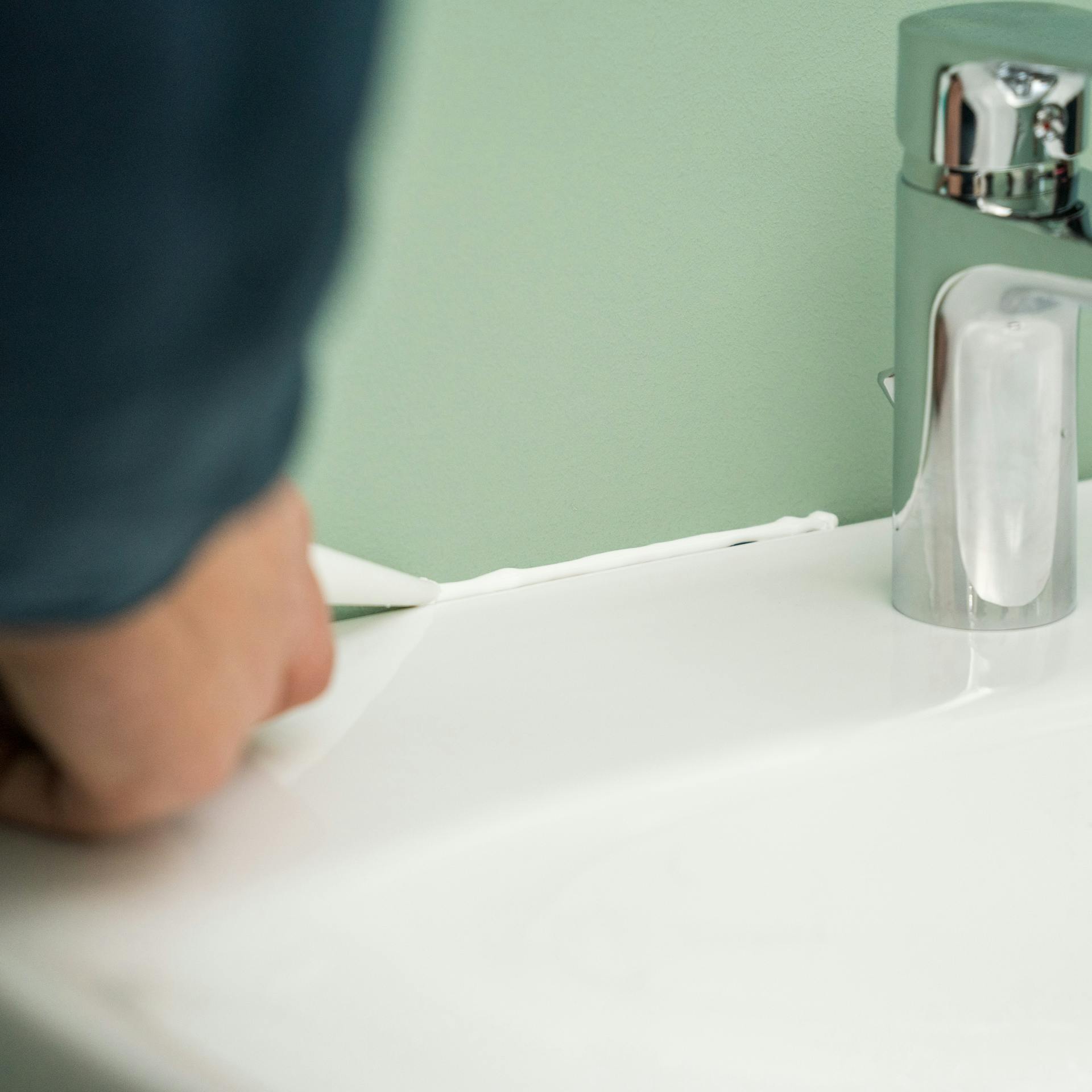 Heimwerker dichtet Übergang von Waschbecken zu Wand mit Silikon ab.