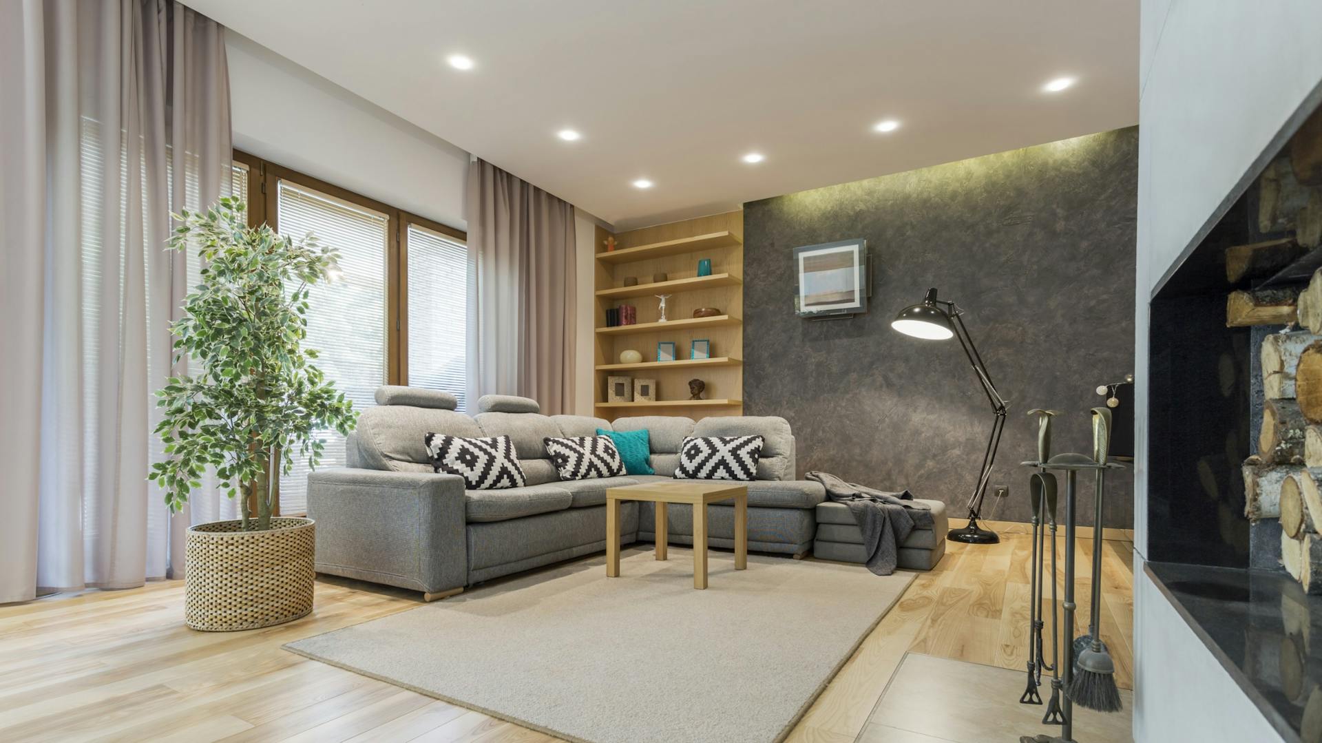 Wohnzimmer mit grauem Sofa, hellem Teppich, Kamin und indirekter Beleuchtung durch Deckenspots