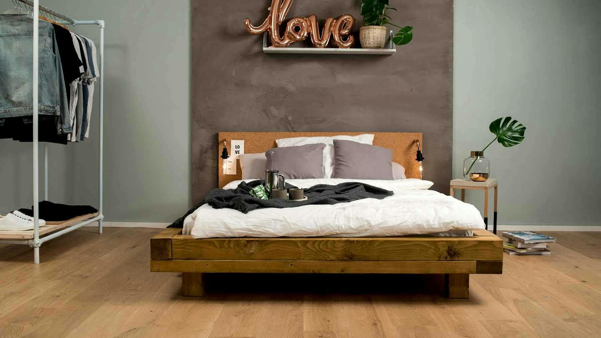 Frontansicht des aus Vollholz bestehenden Bett Ludwig in Eichenfarbe mit Kopfteil vor einer grauen Wand.