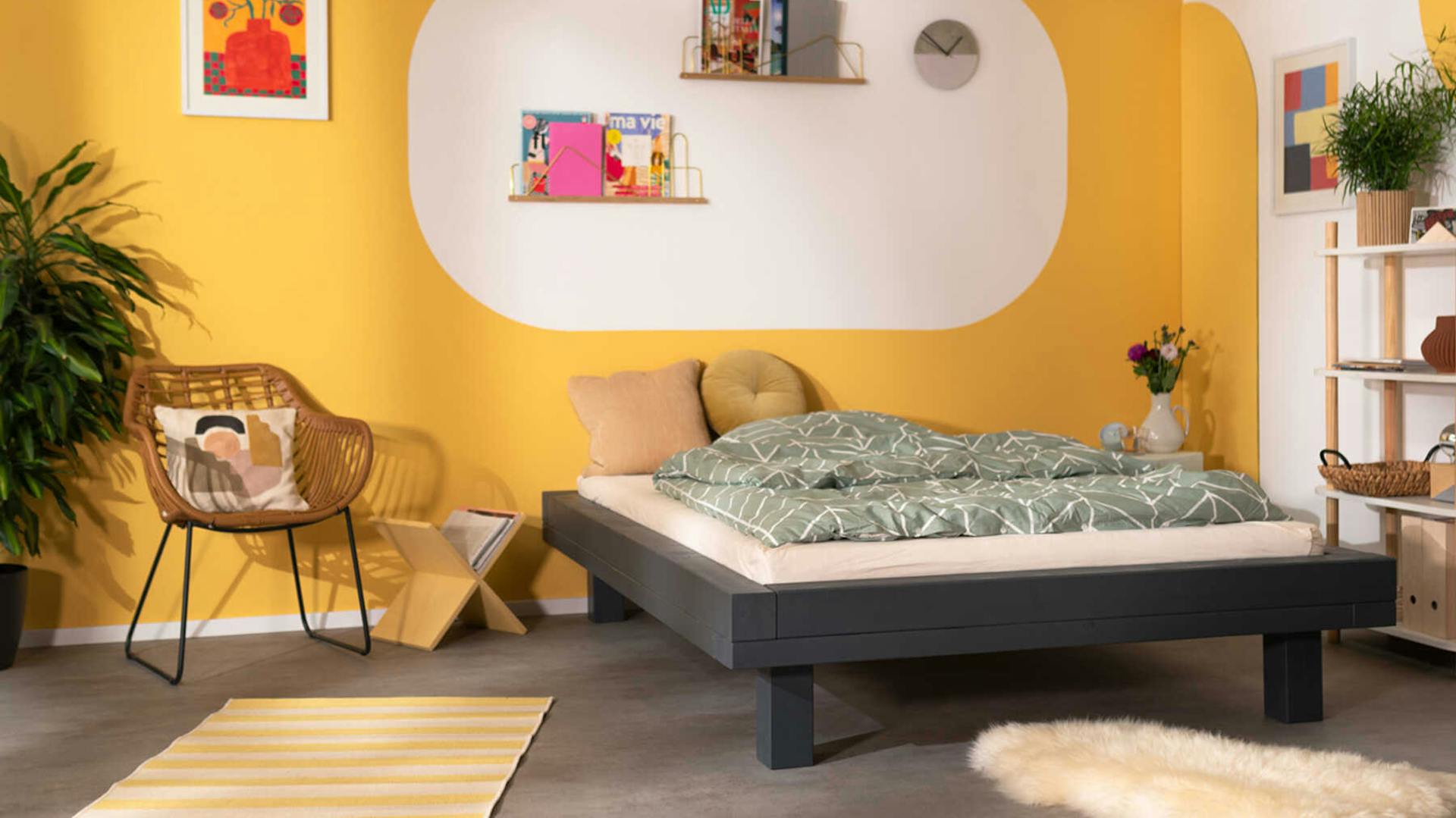 Frontansicht des aus Vollholz bestehenden Bett Ludwig in dunkel grau mit Kopfteil vor einer gelben Wand.