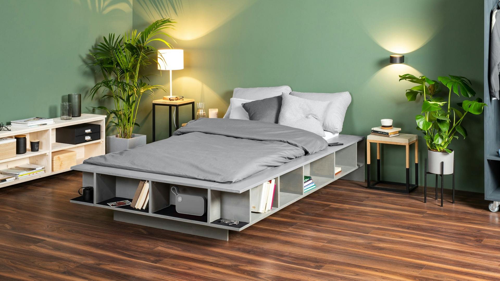 Selbstgebautes Bett mit Regalfächern auf dunklem Holzboden in Schlafzimmer.