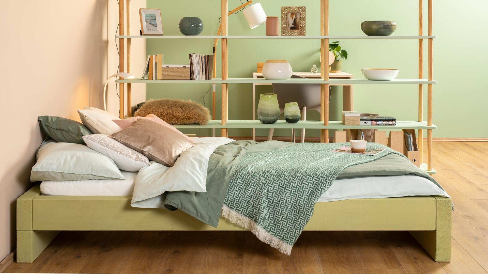 Zöldre festett saját készítésű ágy egy polcos szekrény előtt