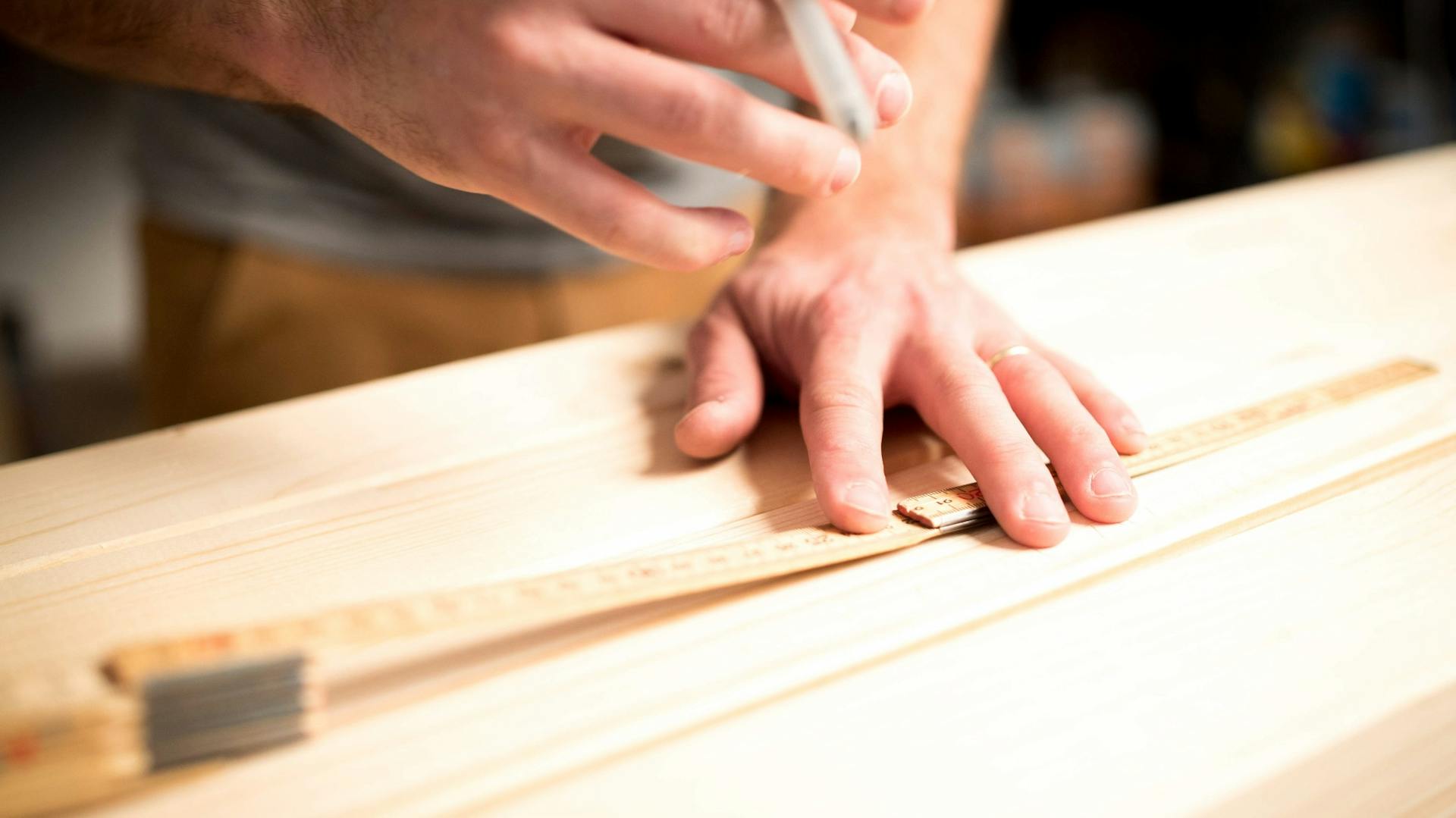 Egy barkácsoló ceruzával és mérőléccel megméri a munkadarabot a fán