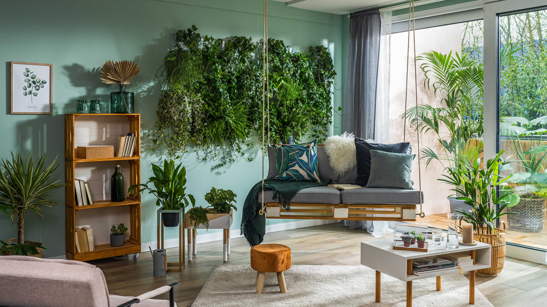 Palettenschaukel Baumelig hängt neben dem Kistenregal in einem Wohnzimmer mit einer bepflanzten Wand.