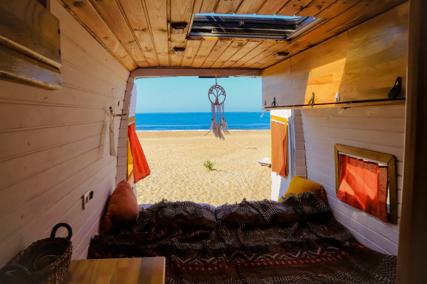 Camper con rivestimento in legno alle pareti e vista su una spiaggia di sabbia