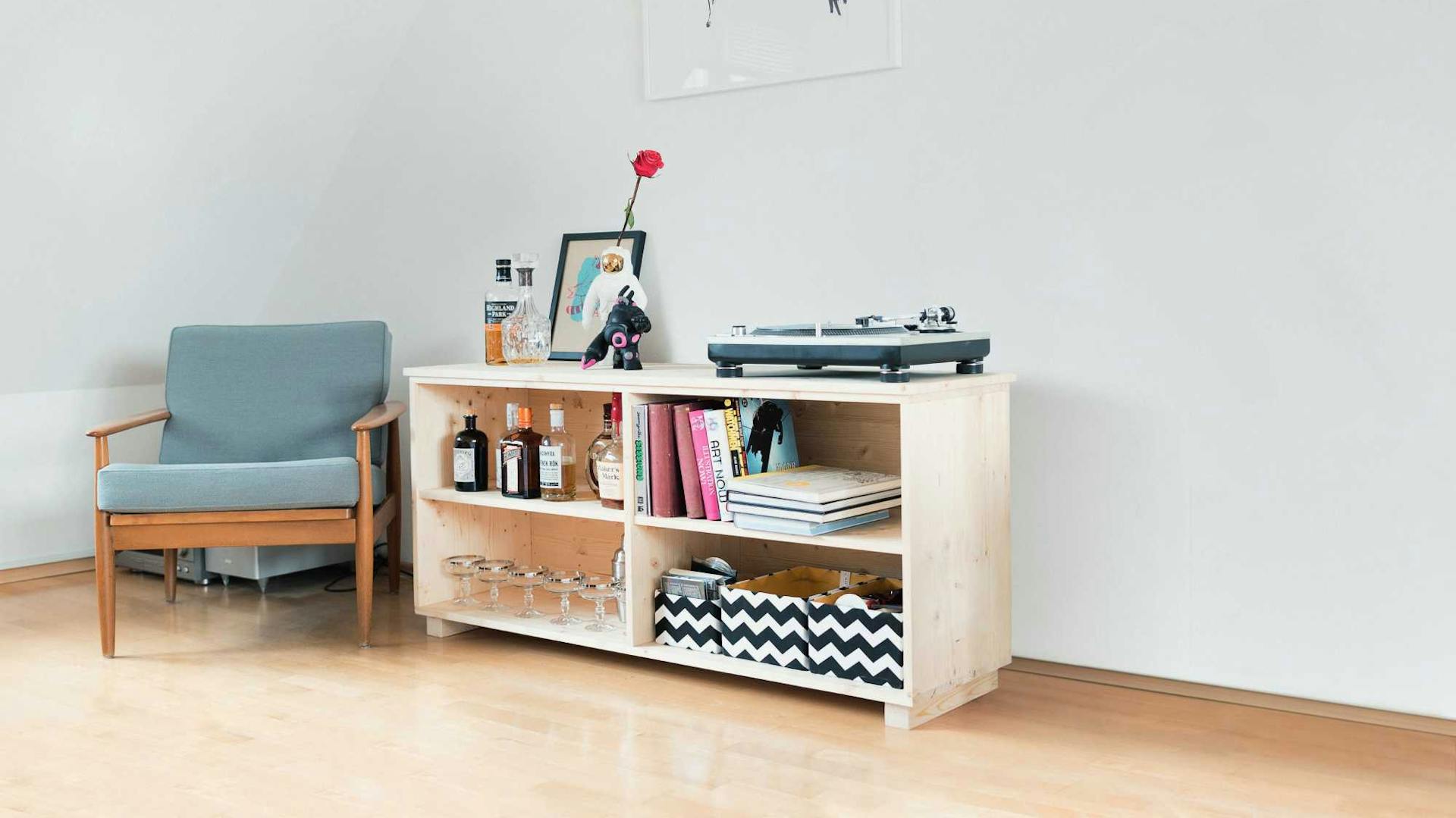 Niedriges Holzregal neben Sessel in Raum mit Dachschräge