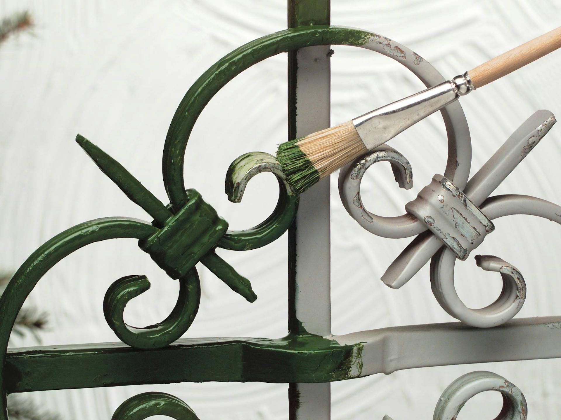 Un elemento metallico di una recinzione viene verniciato di verde con un pennello.