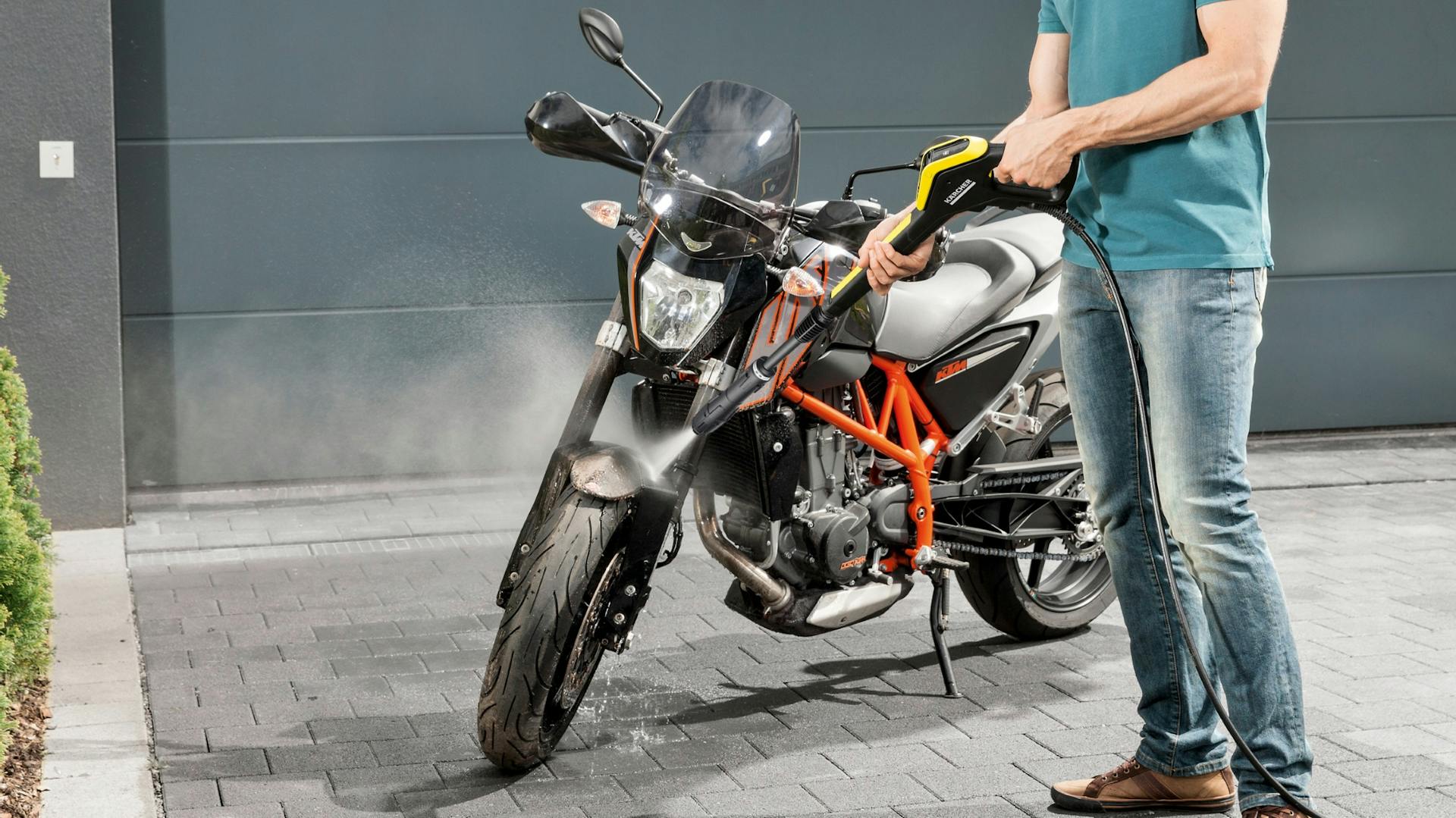 Mann sprengt groben Schmutz von Motorrad mit Hochdruckreiniger ab