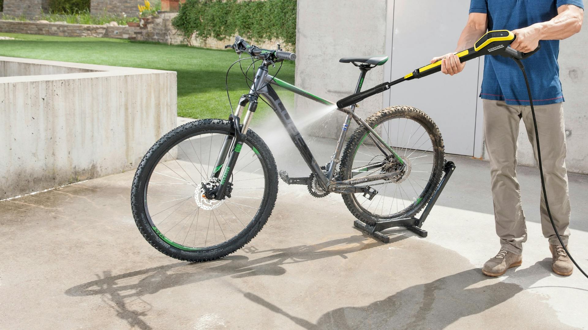 Mann sprüht groben Schmutz von Fahrrad mit Hochdruckreiniger ab