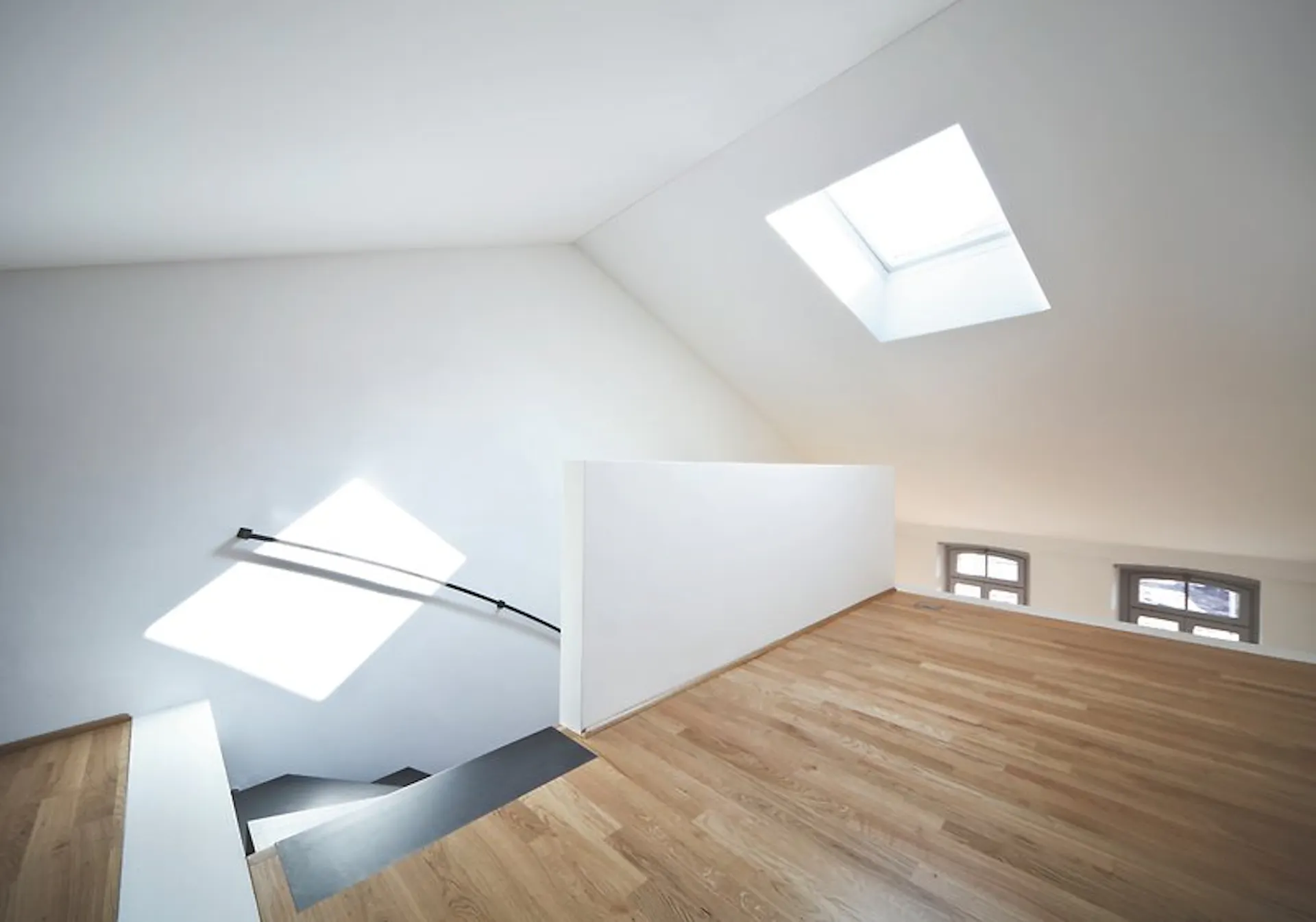 Raum mit weissen Wänden und schräger Decke sowie Holzboden und Fenster.