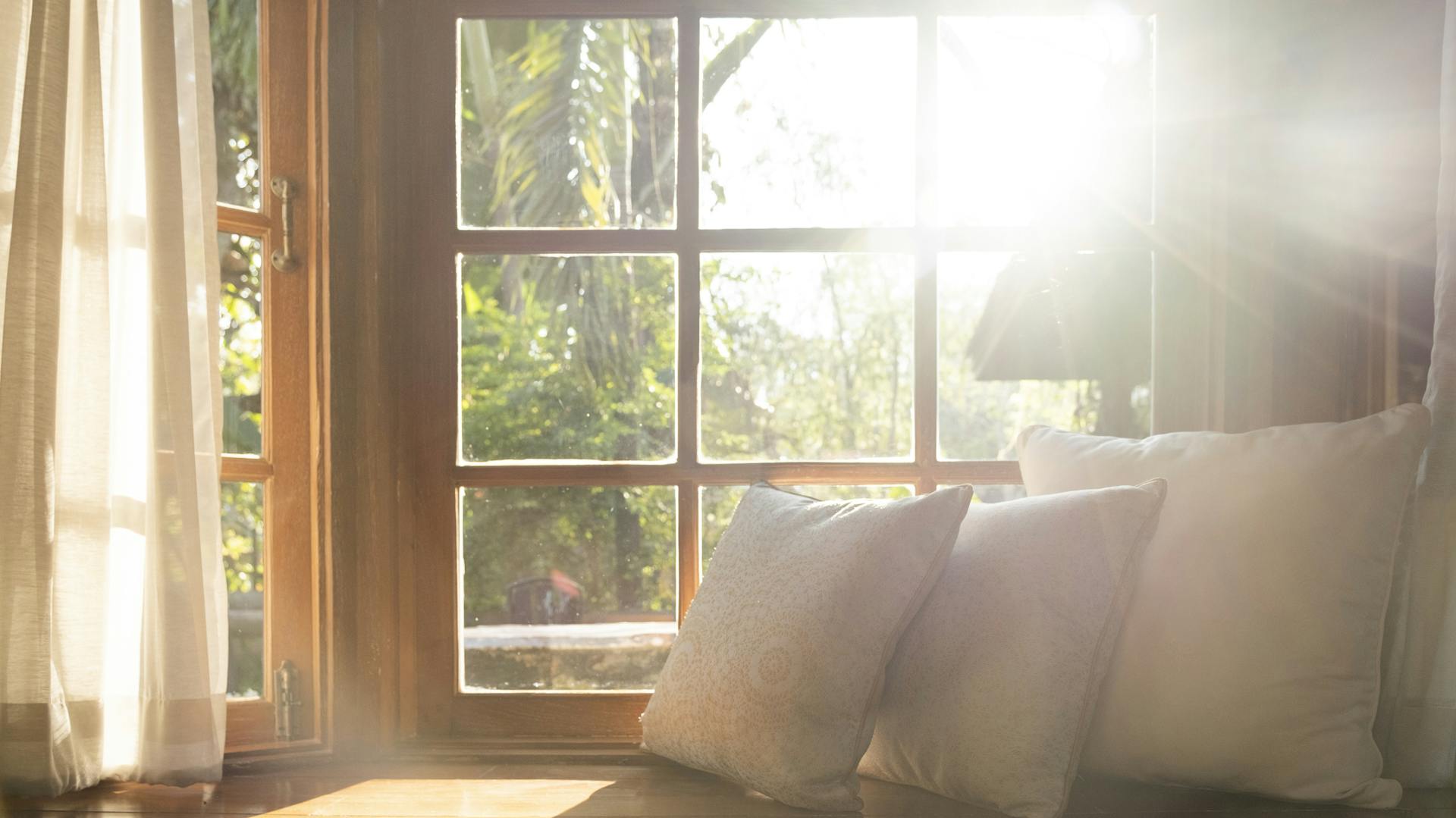 Durch ein grroßes Fenster mit einem Kissen davor strahlt die Sonne.