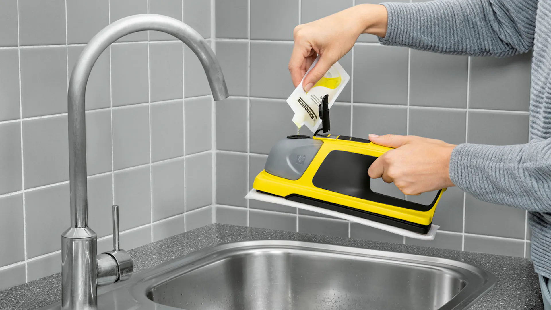 Někdo plní před čištěním oken čisticí prostředek do akumulátorového vysavače.