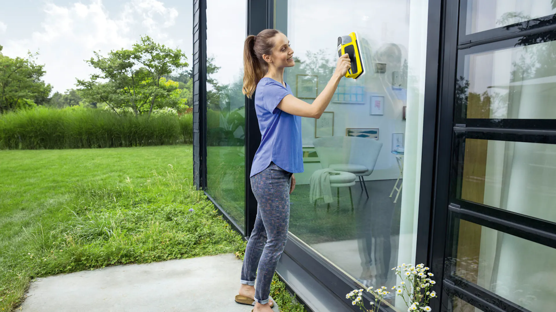Žena čistí okna zevnitř pomocí akumulátorové stěrky.