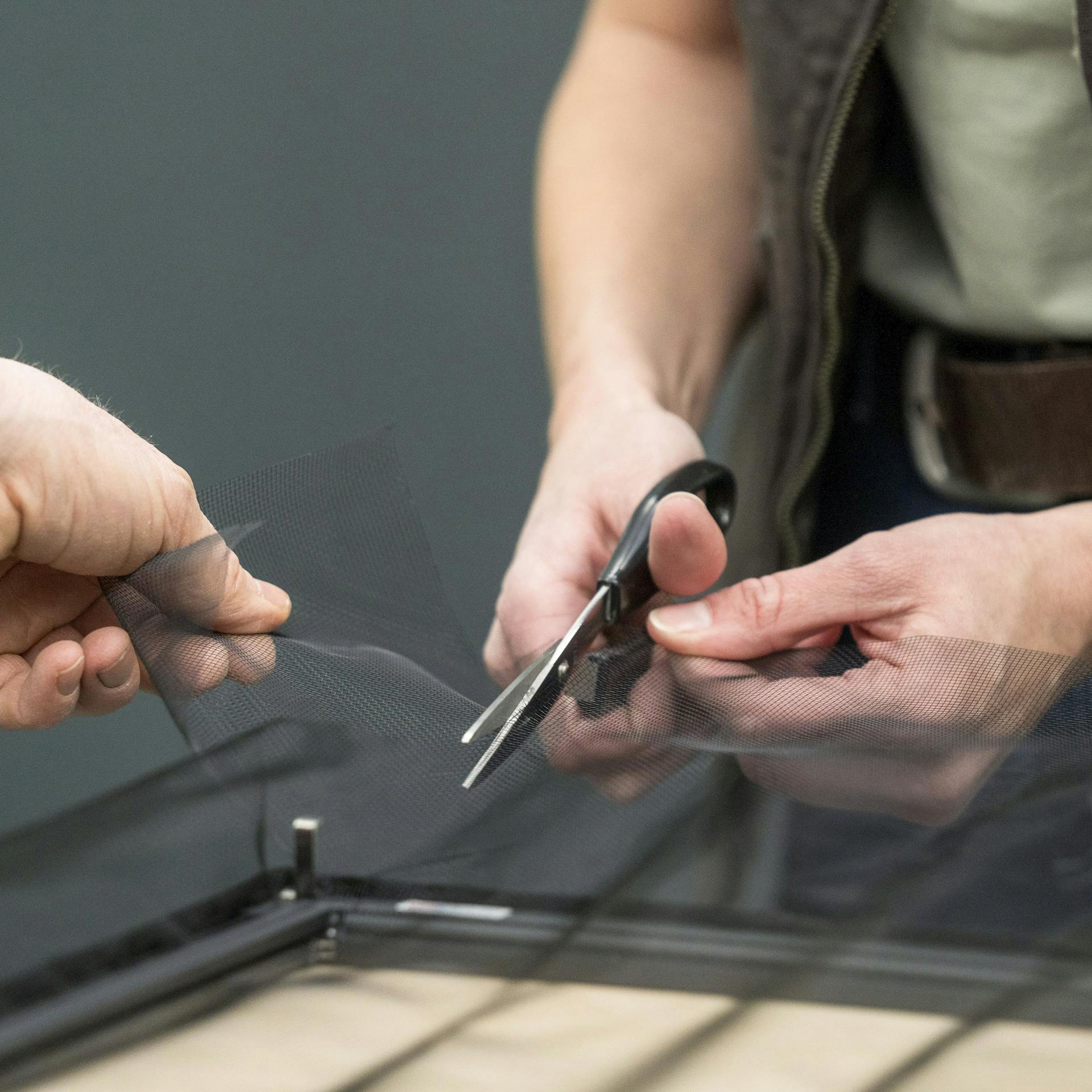 Handwerker schneiden das Netz des Fliegengitters zu.