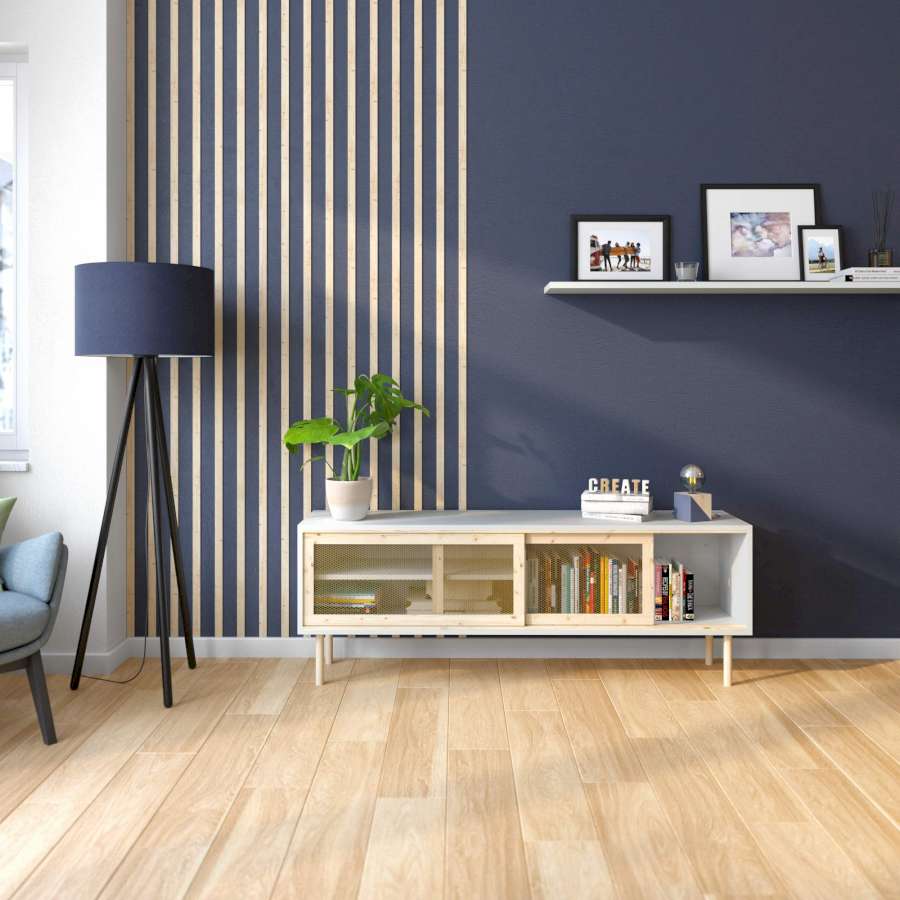 Eine dunkelblaue Wand wurde zur Hälfte mit senkrechten Holzleisten gestaltet. An der anderen Seite ist eine Bilderleiste angebracht. Vor der Wand stehen eine blaue Lampe und ein kleines Regal.