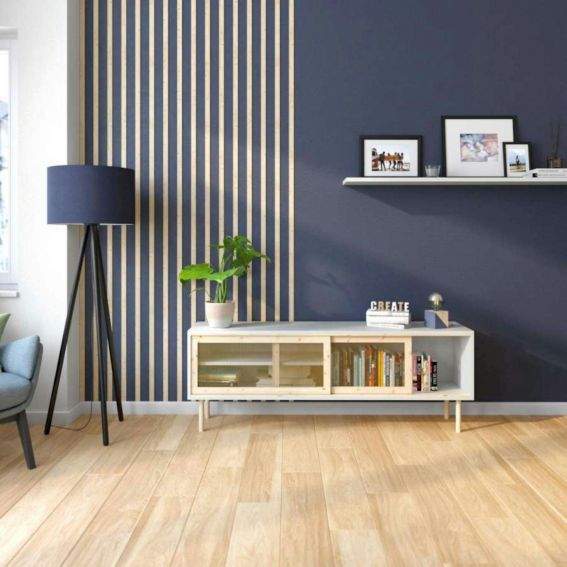 Eine dunkelblaue Wand wurde zur Hälfte mit senkrechten Holzleisten gestaltet. An der anderen Seite ist eine Bilderleiste angebracht. Vor der Wand stehen eine blaue Lampe und ein kleines Regal.