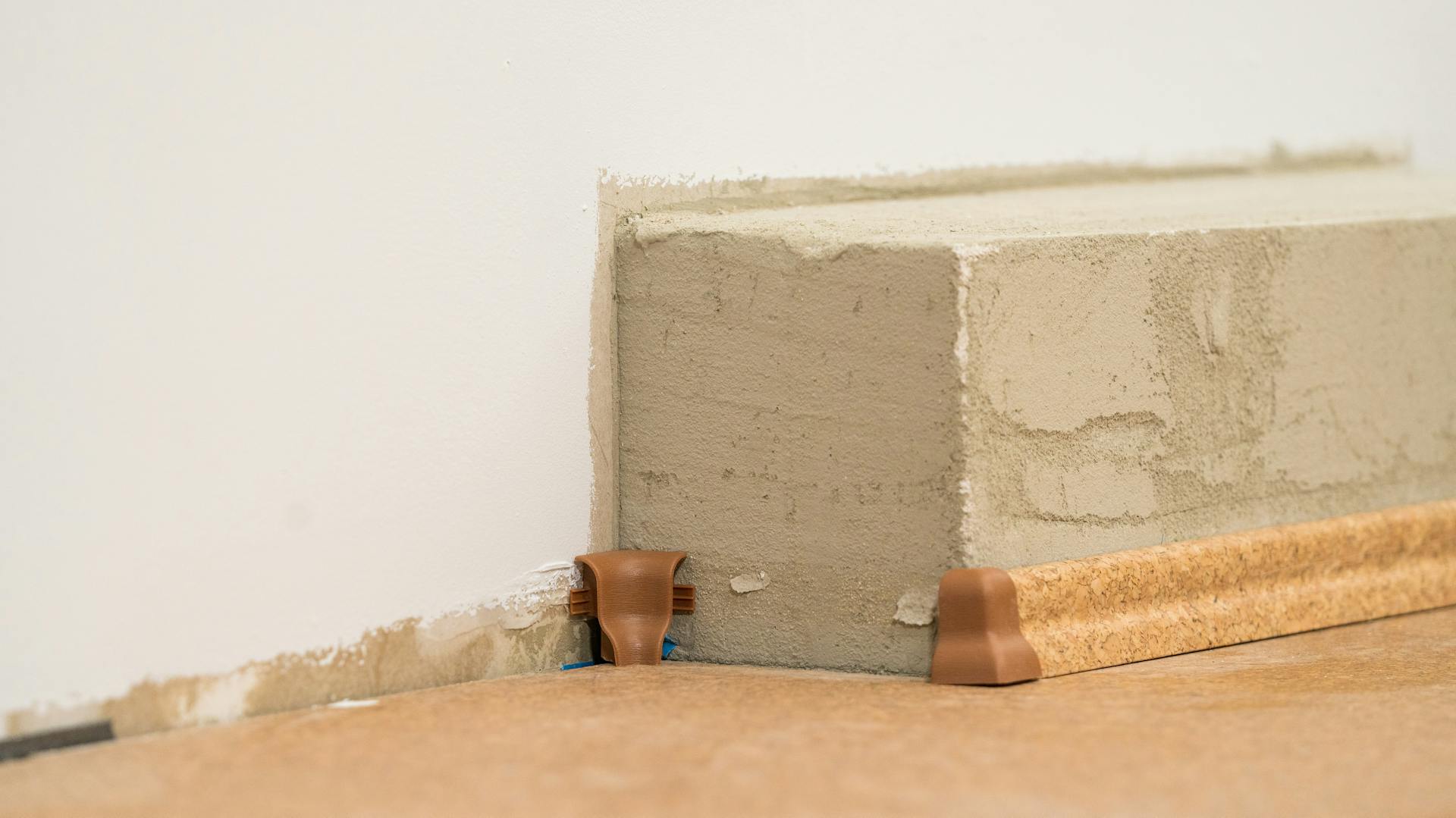 Handwerker befestigt eine Fußleiste mit einem Eckverbinder.