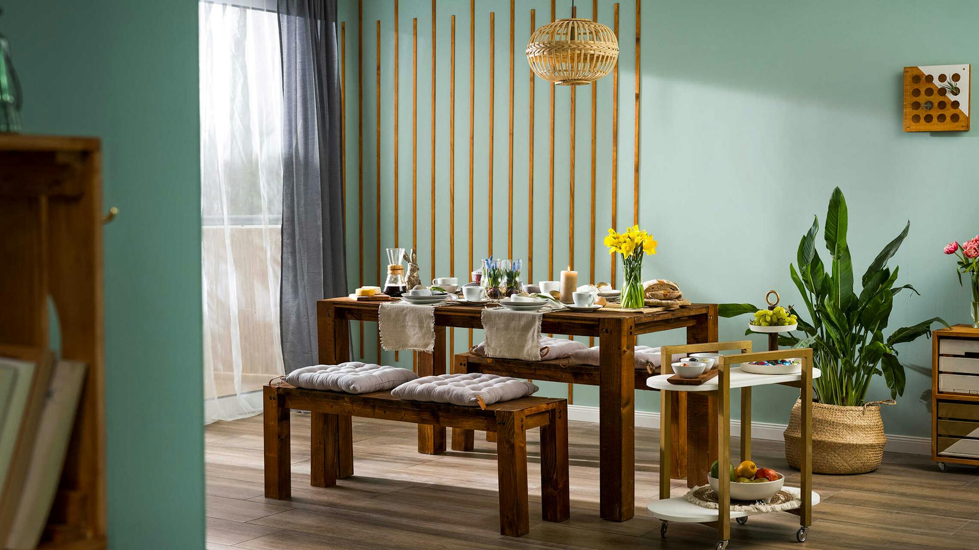 Tisch Maren aus dunklem Holz ist feierlich zu Ostern gedeckt und steht vor einer Wand, die mit Leisten gestaltet worden ist.