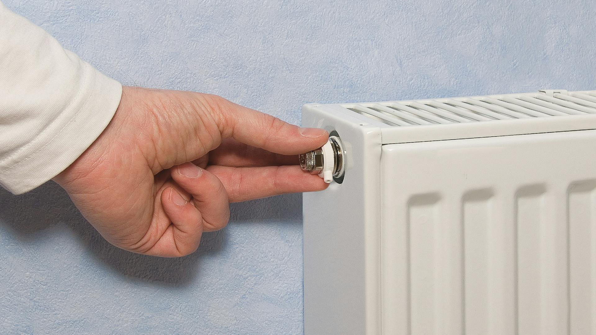 Hand dreht an dem Entlüftungsventil eines weißen Heizkörpers.