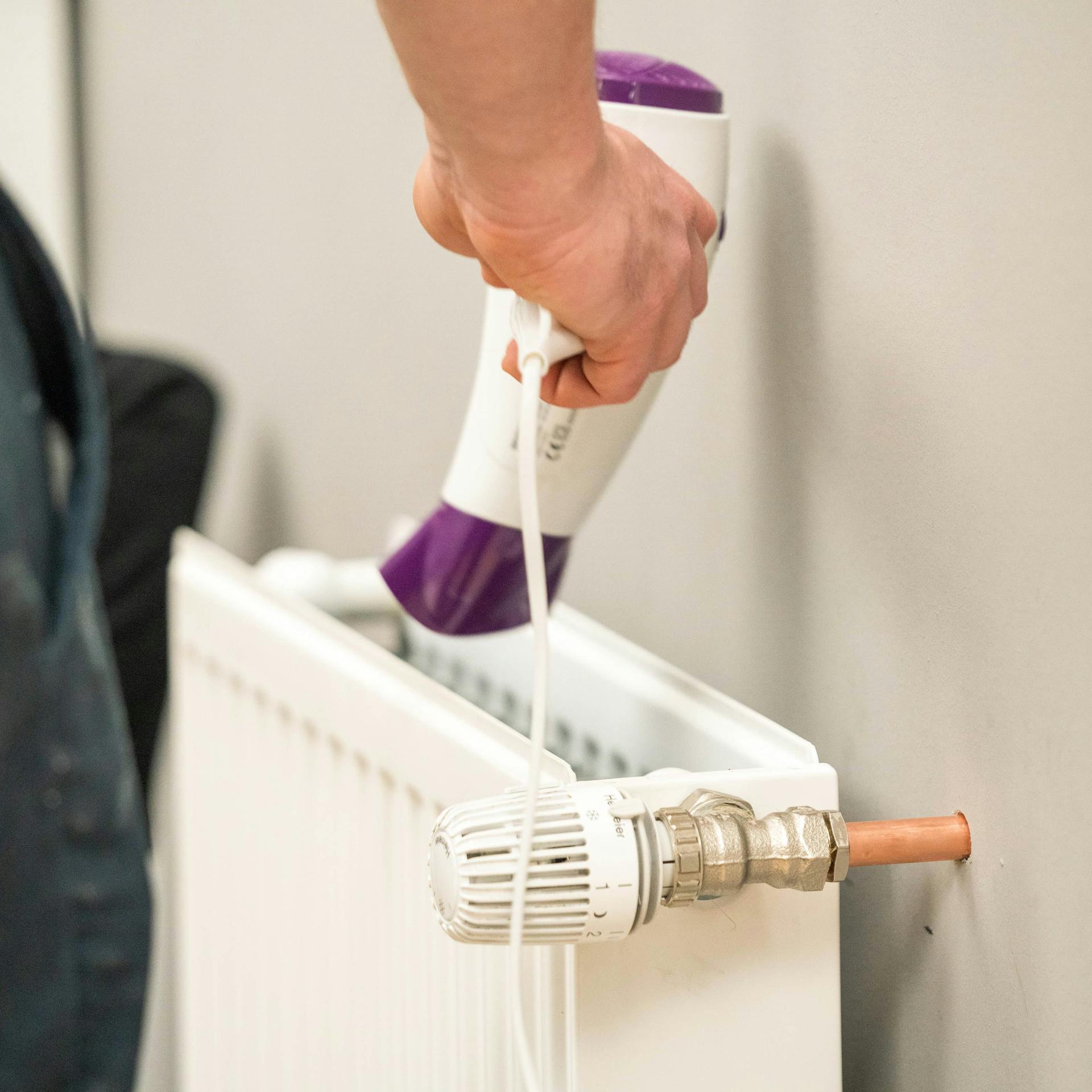 Egy férfi hajszárítóval tisztítja a radiátor belsejét.