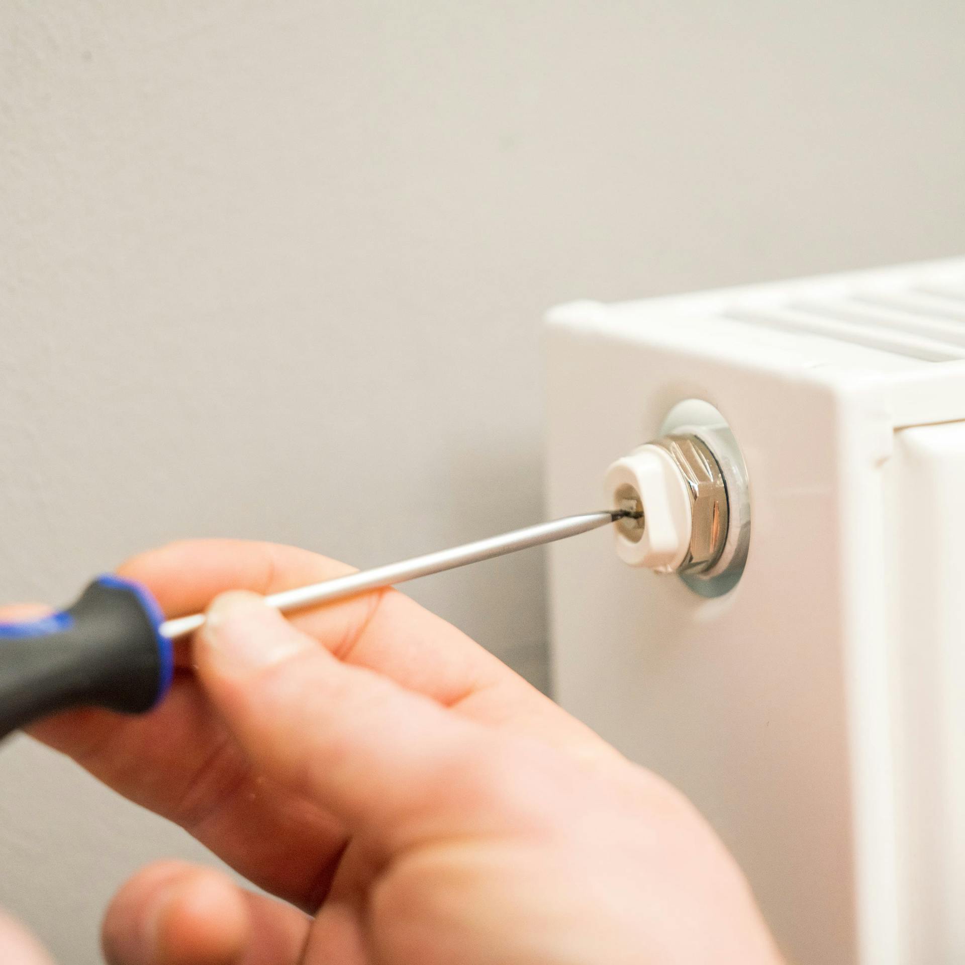 A férfi csavarhúzóval elzárja egy radiátor szelepét.