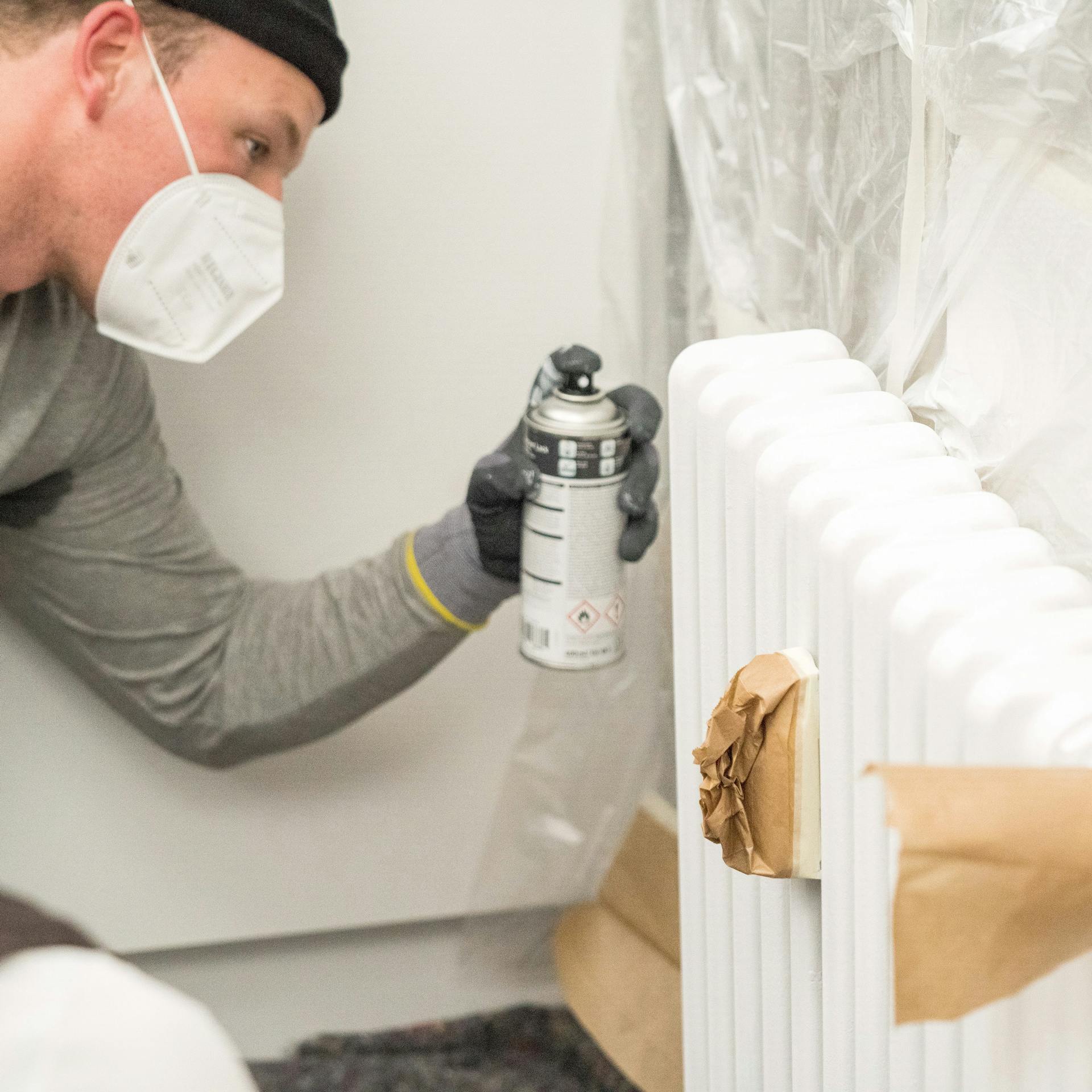 Egy barkácsoló festéket permetez egy radiátorra.