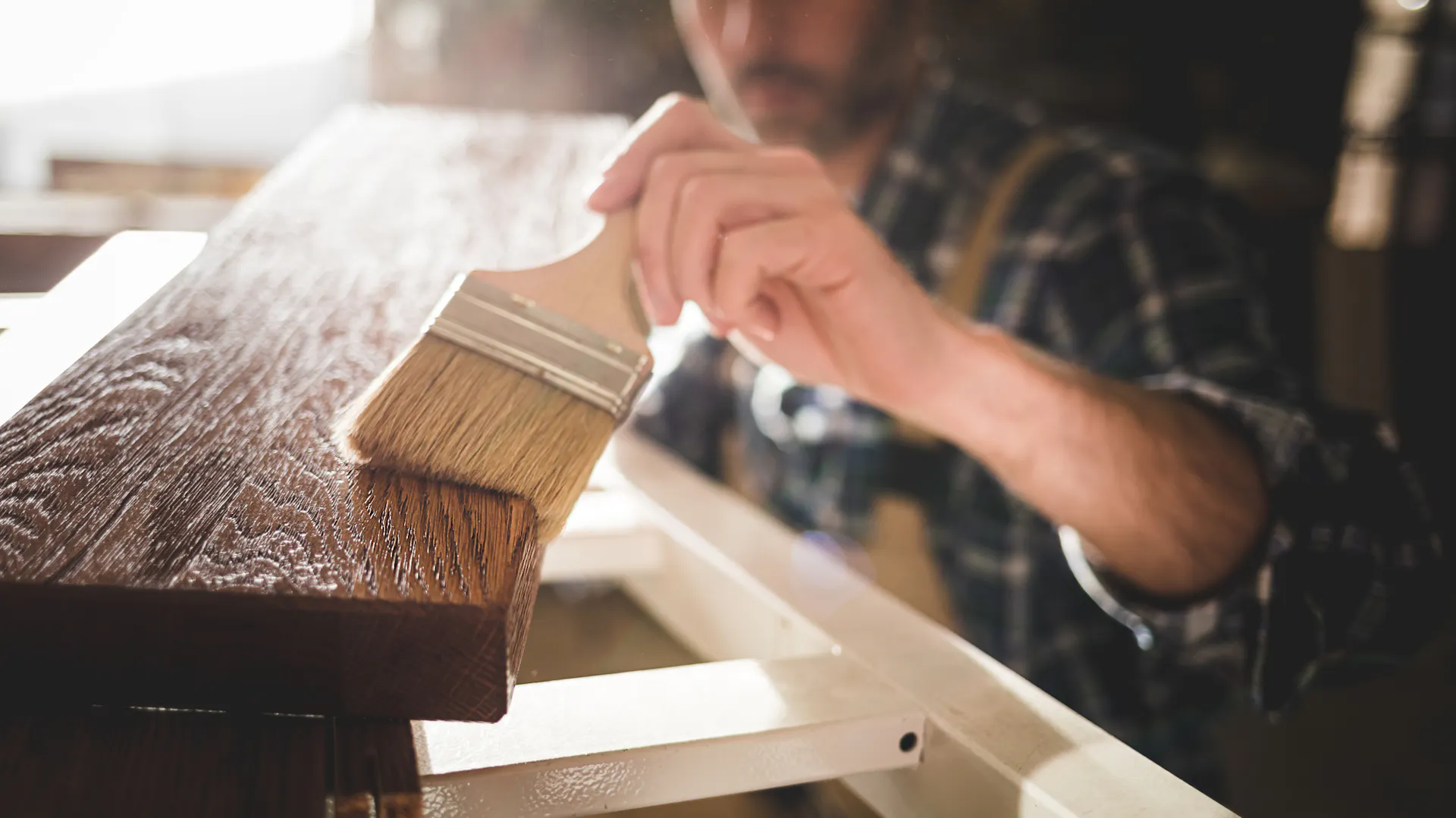 Egy barkácsoló lazúrt visz fel a deszkára ecsettel.