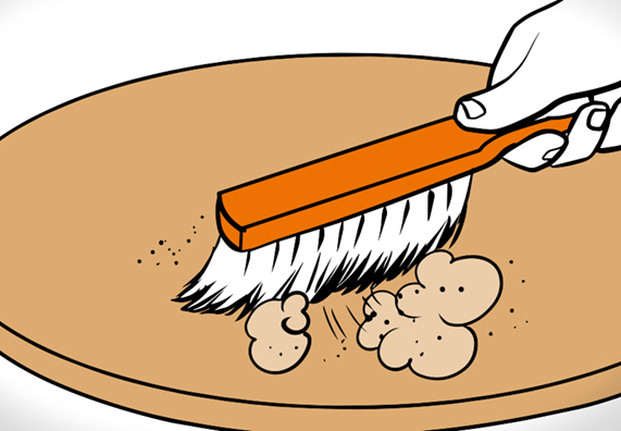 Hand mit Handfeger auf Holztisch